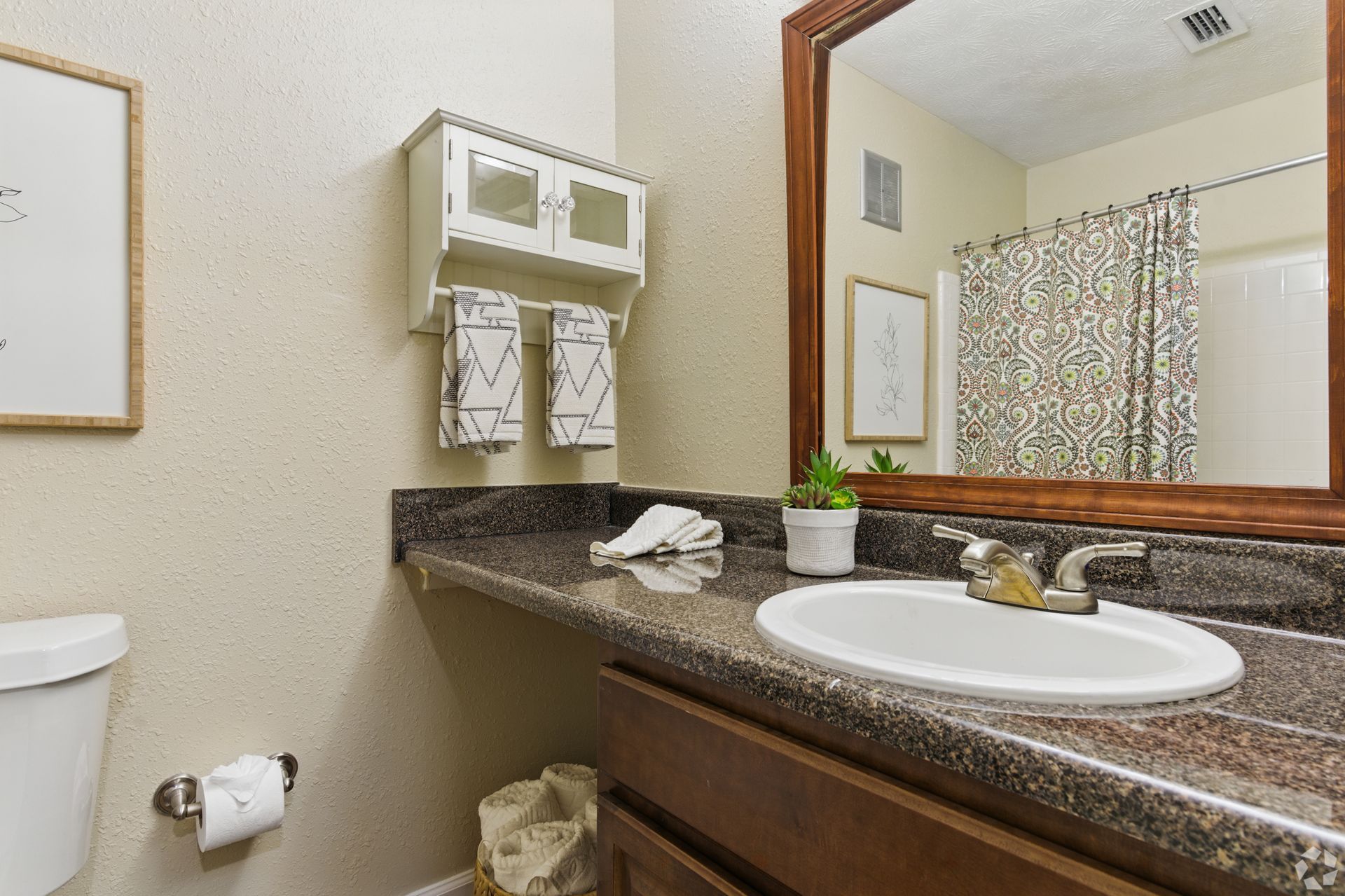 Bathroom with a brown countertop, white sink, and dark-framed mirror. White cabinet above countertop, with towels hanging.