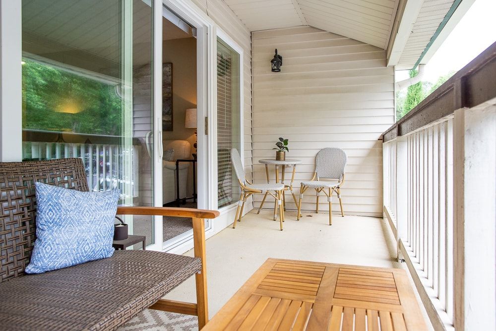 A balcony with a wooden table , chairs and a couch at Kinstone River Apartment Homes, offering 1, 2, and 3 bedroom apartments for rent near I-285 in Atlanta, GA.