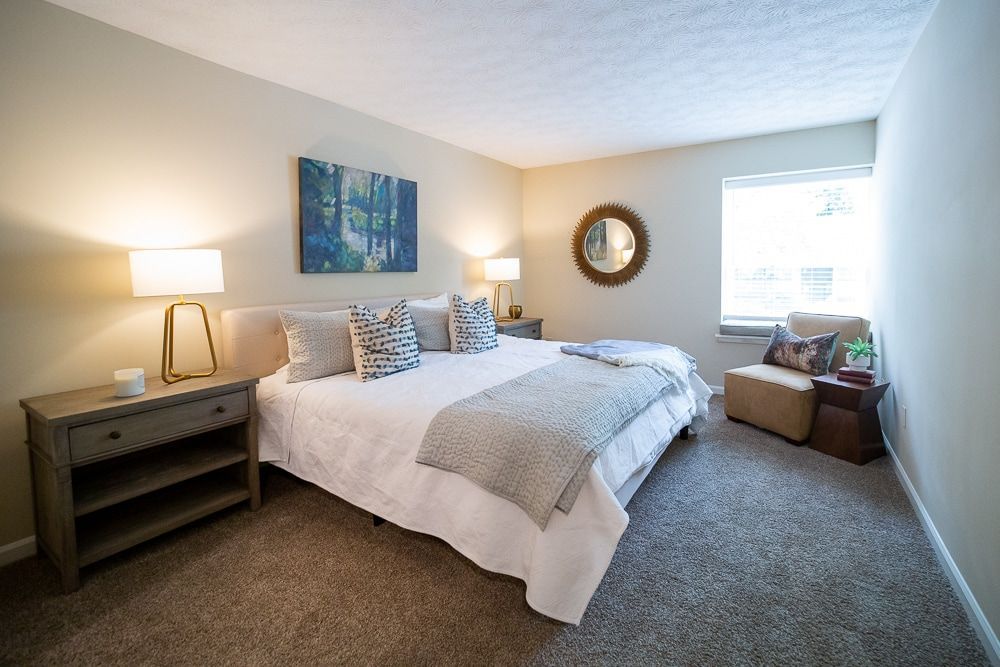 A bedroom with a large bed, nightstands, lamps, and a chair at Kinstone River, offering apartments near Cumberland Mall.