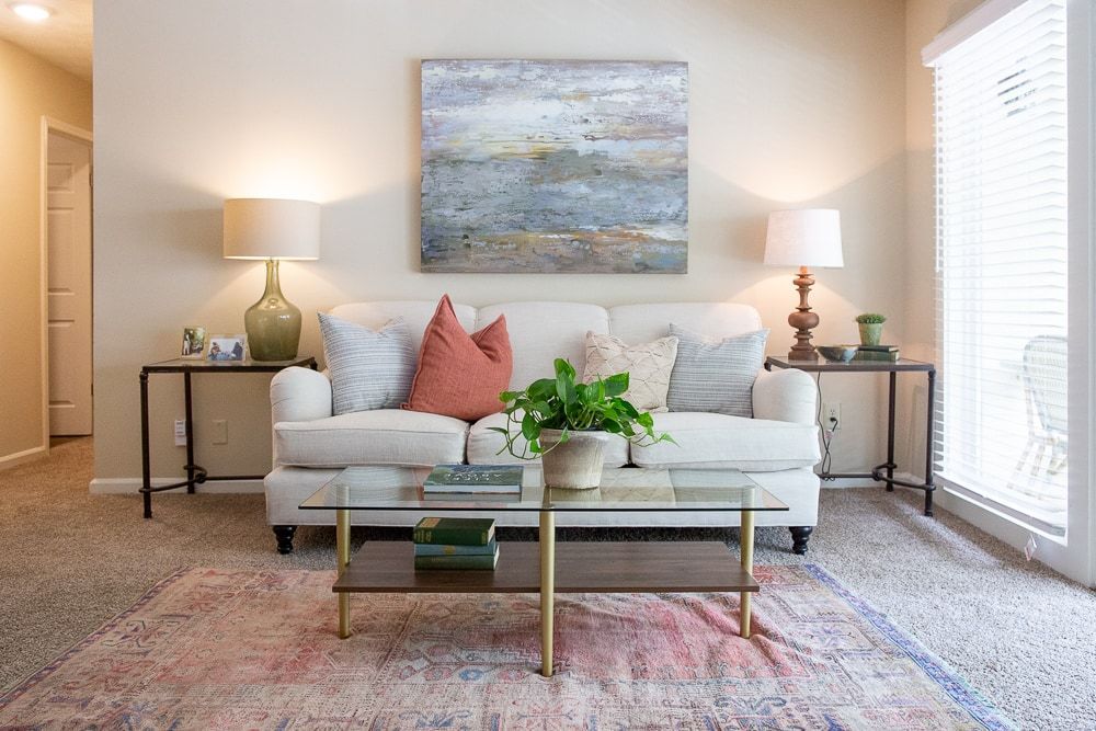 A living room with a couch, coffee table, lamps, and a painting on the wall at Kinstone River, offering apts in Atlanta, GA.