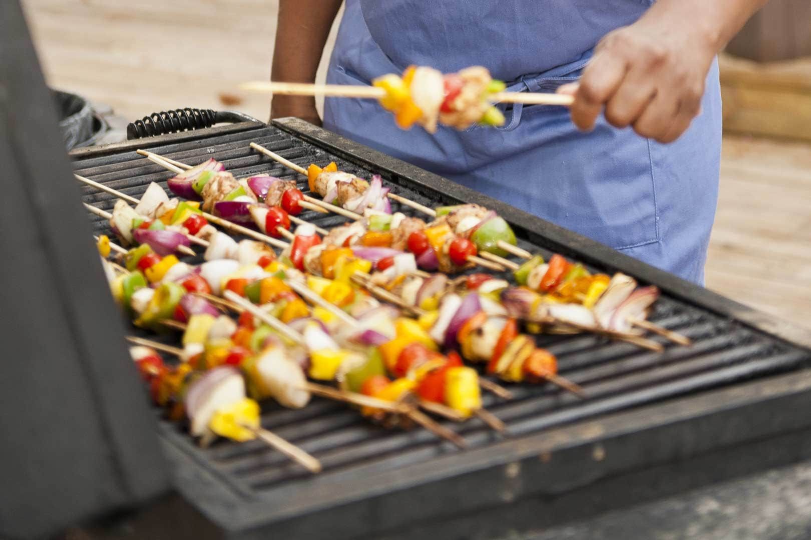 A person is grilling vegetables on skewers on a grill.