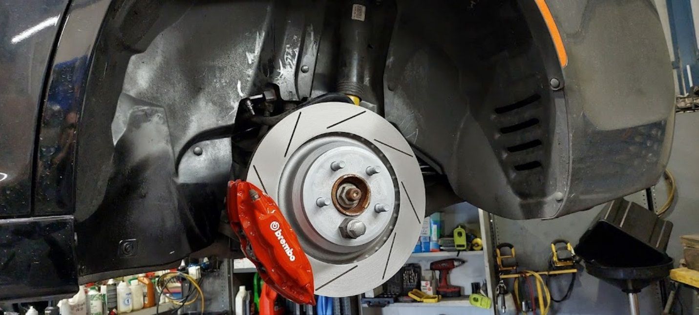 A Car With A Red Brake Caliper Is Sitting On A Lift In A Garage — Albion Park Auto Electrical & Mechanical In  Albion Park Rail, NSW