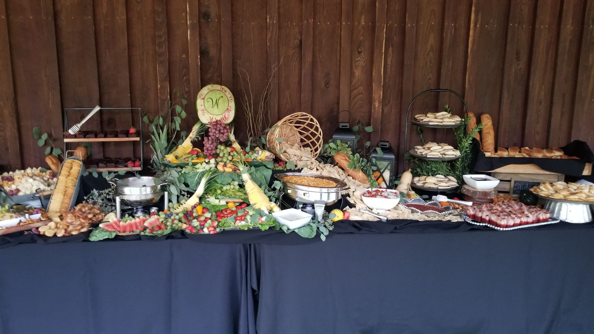 A buffet table with lots of food on it in front of a wooden wall.