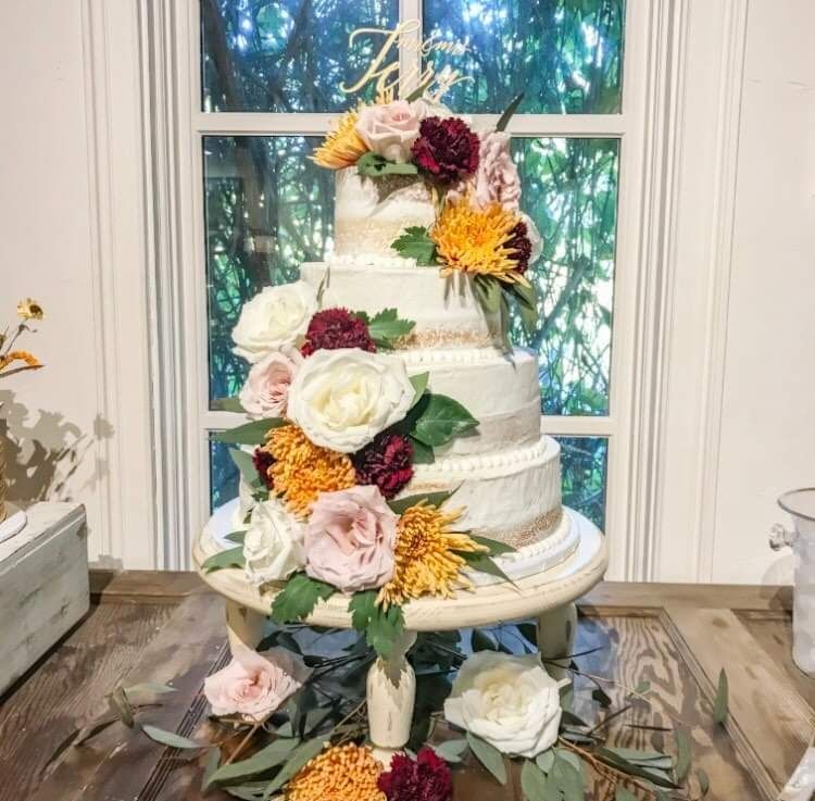 A wedding cake with flowers on it is sitting on a table in front of a window.