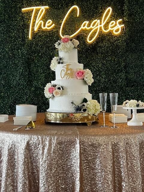A wedding cake is sitting on a table in front of a neon sign that says the cagles.