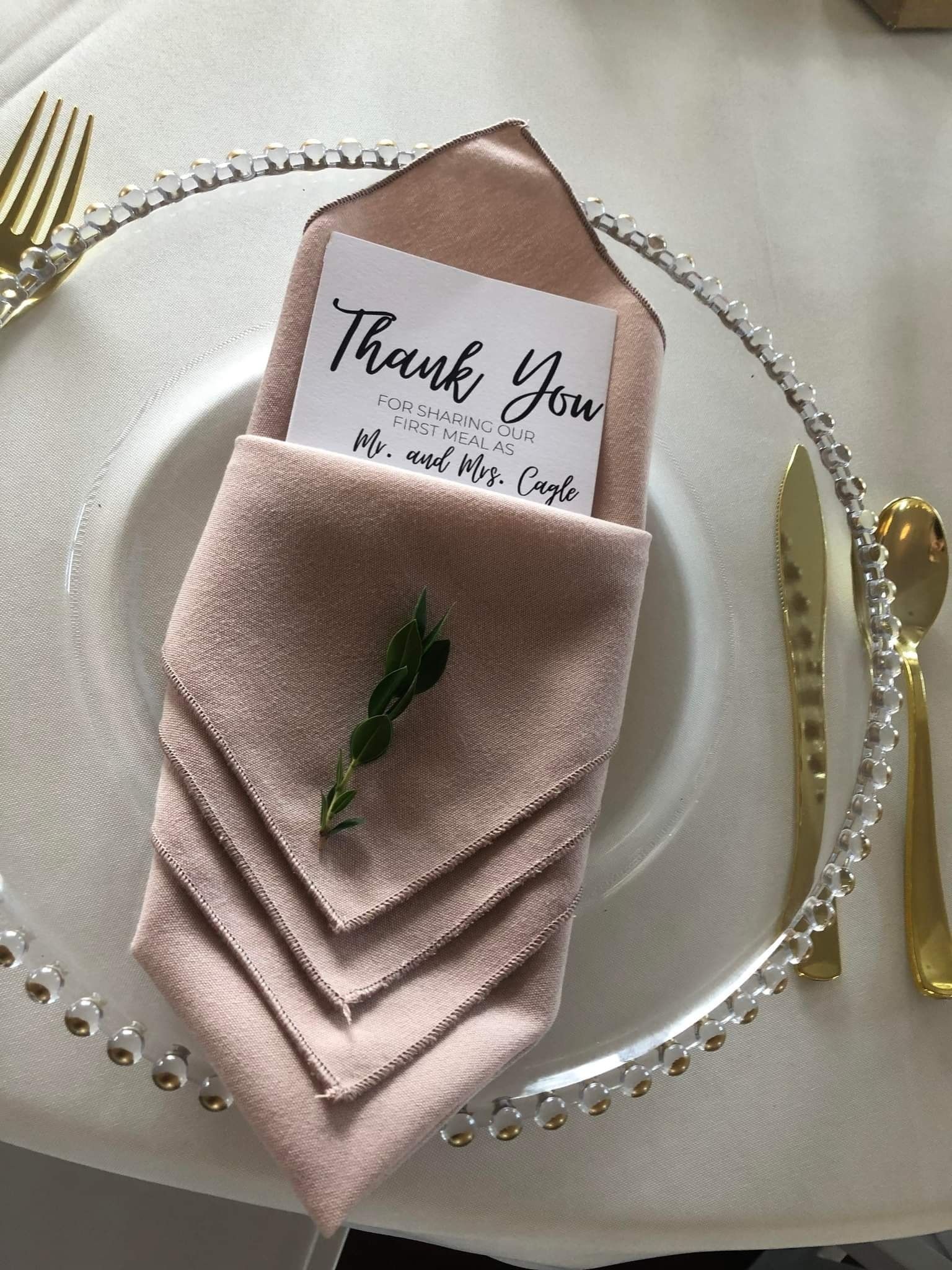 A thank you card is folded into a napkin on a plate.
