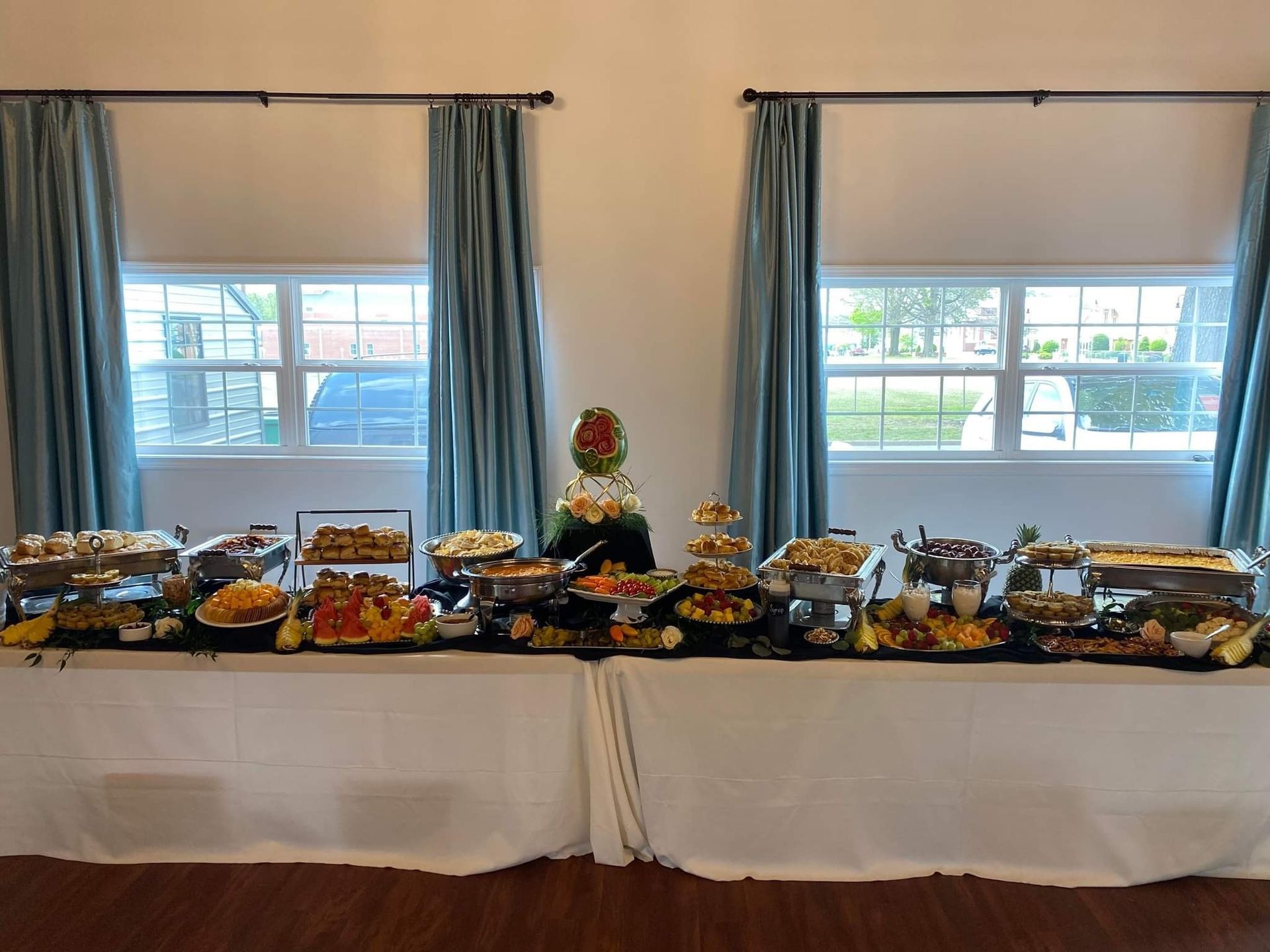 A long buffet table filled with lots of food in front of two windows.