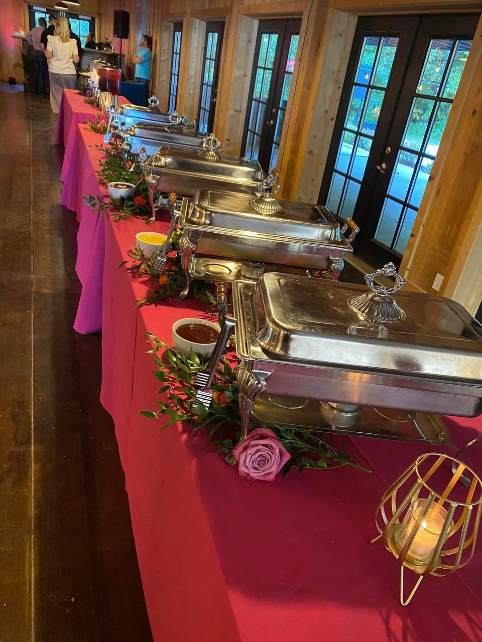 A long table with a pink tablecloth and a bunch of buffet trays on it.