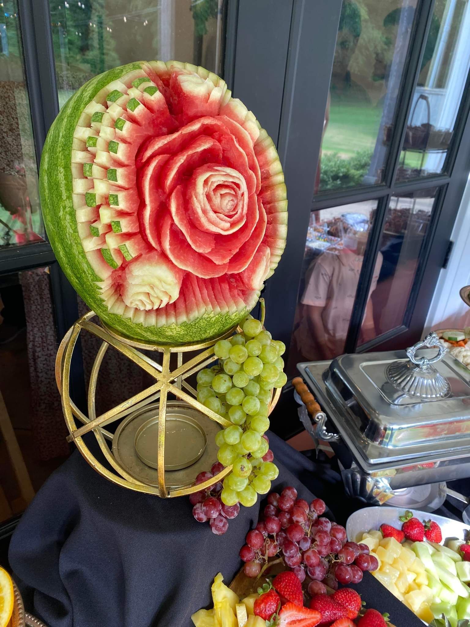 A watermelon carved into a rose is sitting on top of a buffet table.