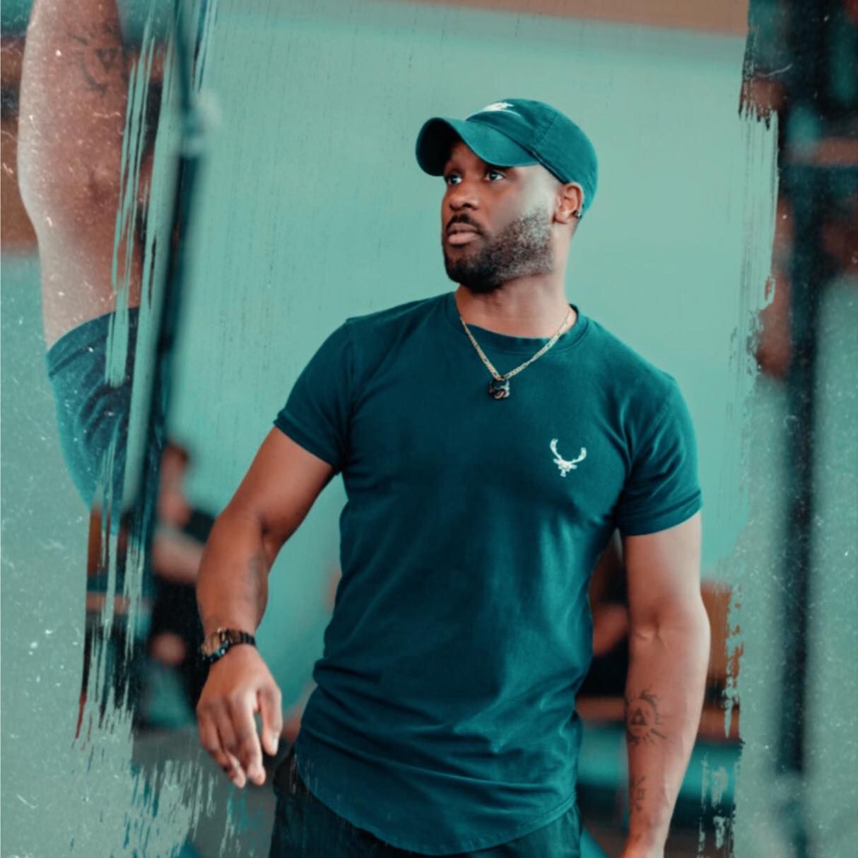 A person wearing a green baseball cap and matching t-shirt with a small emblem, looking off to the side.