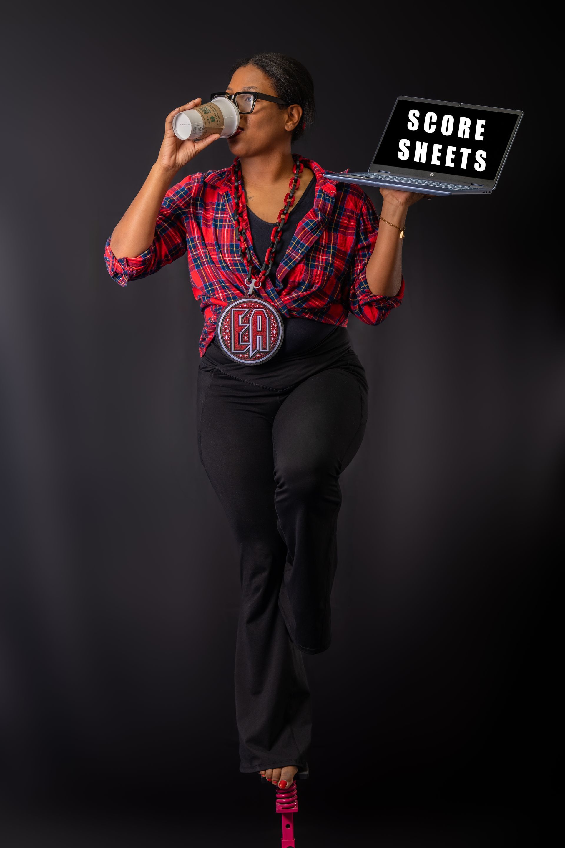 A person drinking from a cup while balancing on one leg, holding a laptop displaying the text 