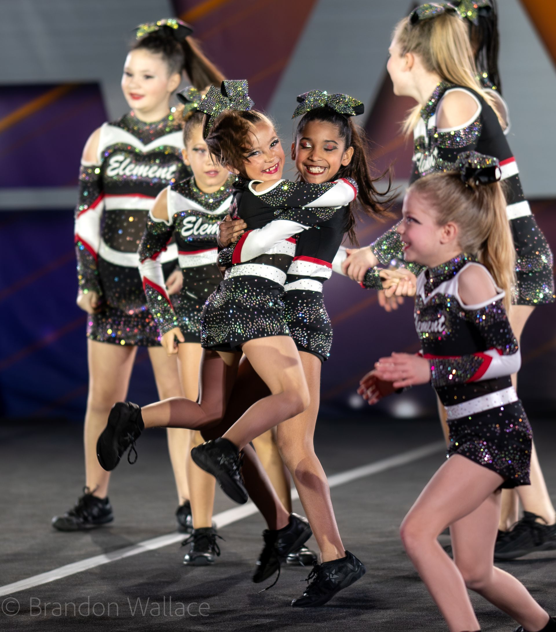 A group of cheerleaders in matching black and sequined uniforms celebrate on a competition mat.