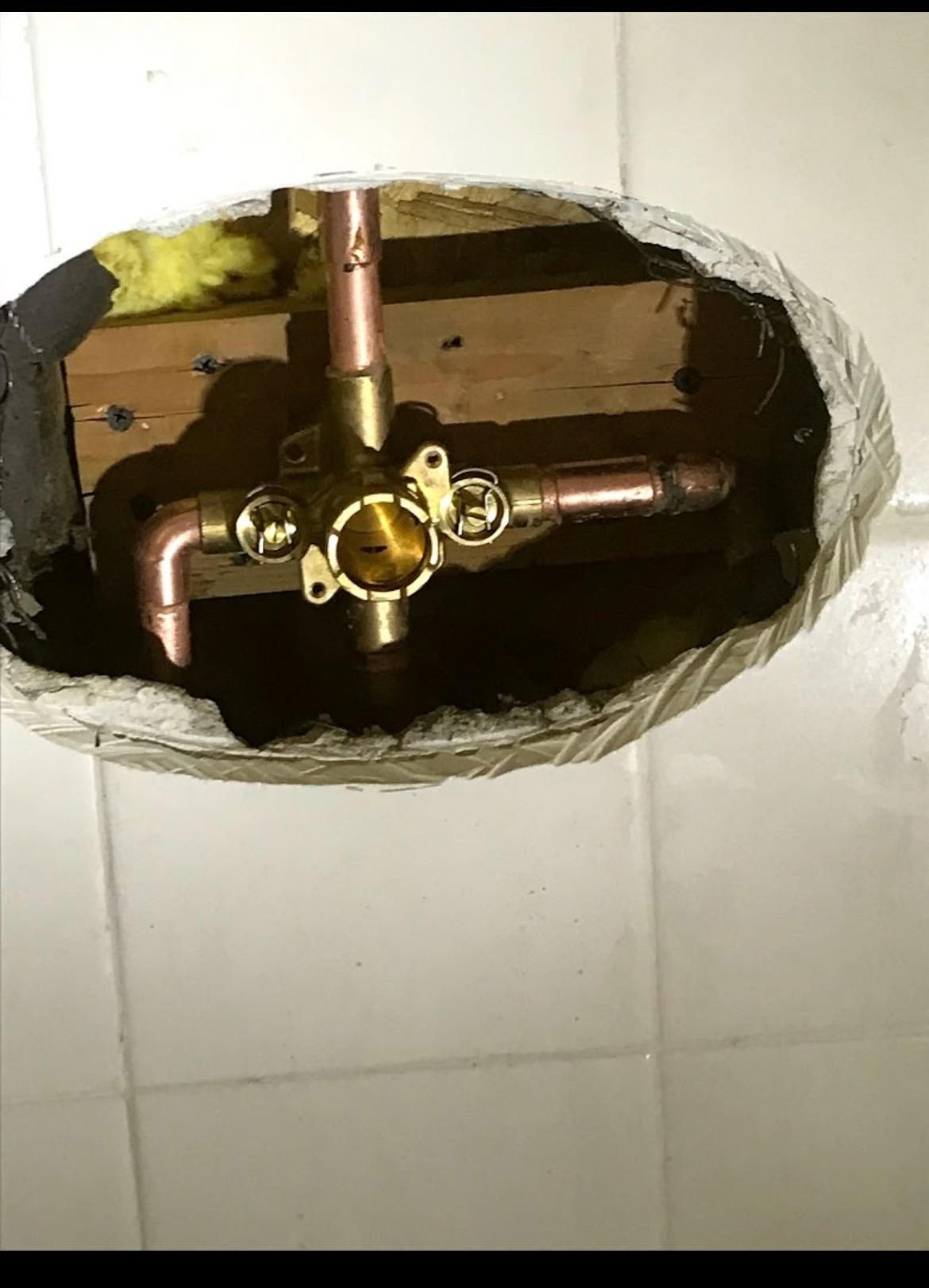 Copper plumbing fixtures inside a bathroom wall; yellow insulation, white tiles.