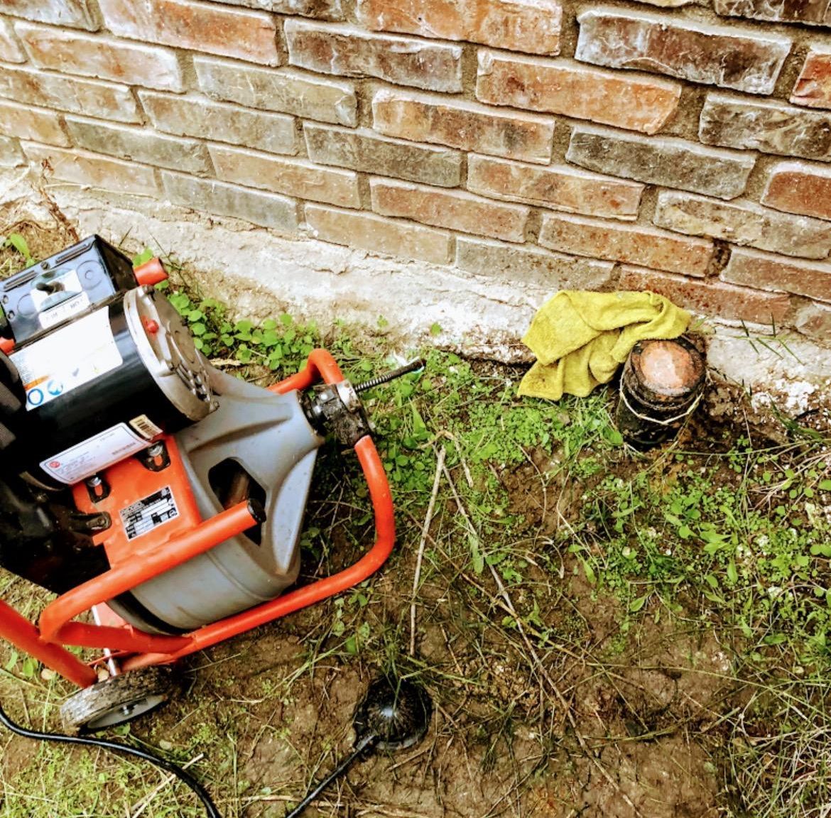 A plumbing snake machine next to a brick wall, clearing a drain.