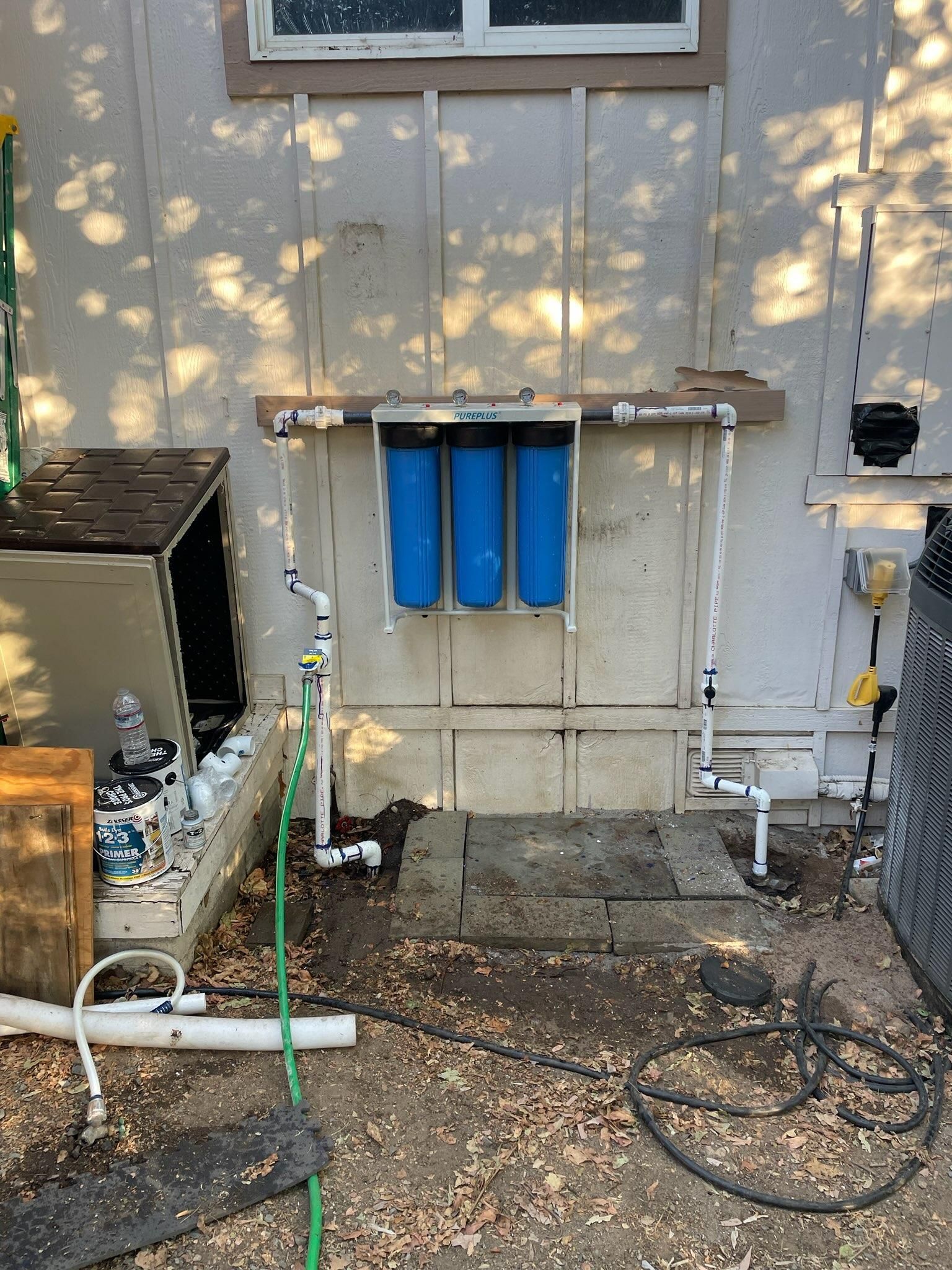 Blue water filtration system on the exterior of a home with white PVC piping.