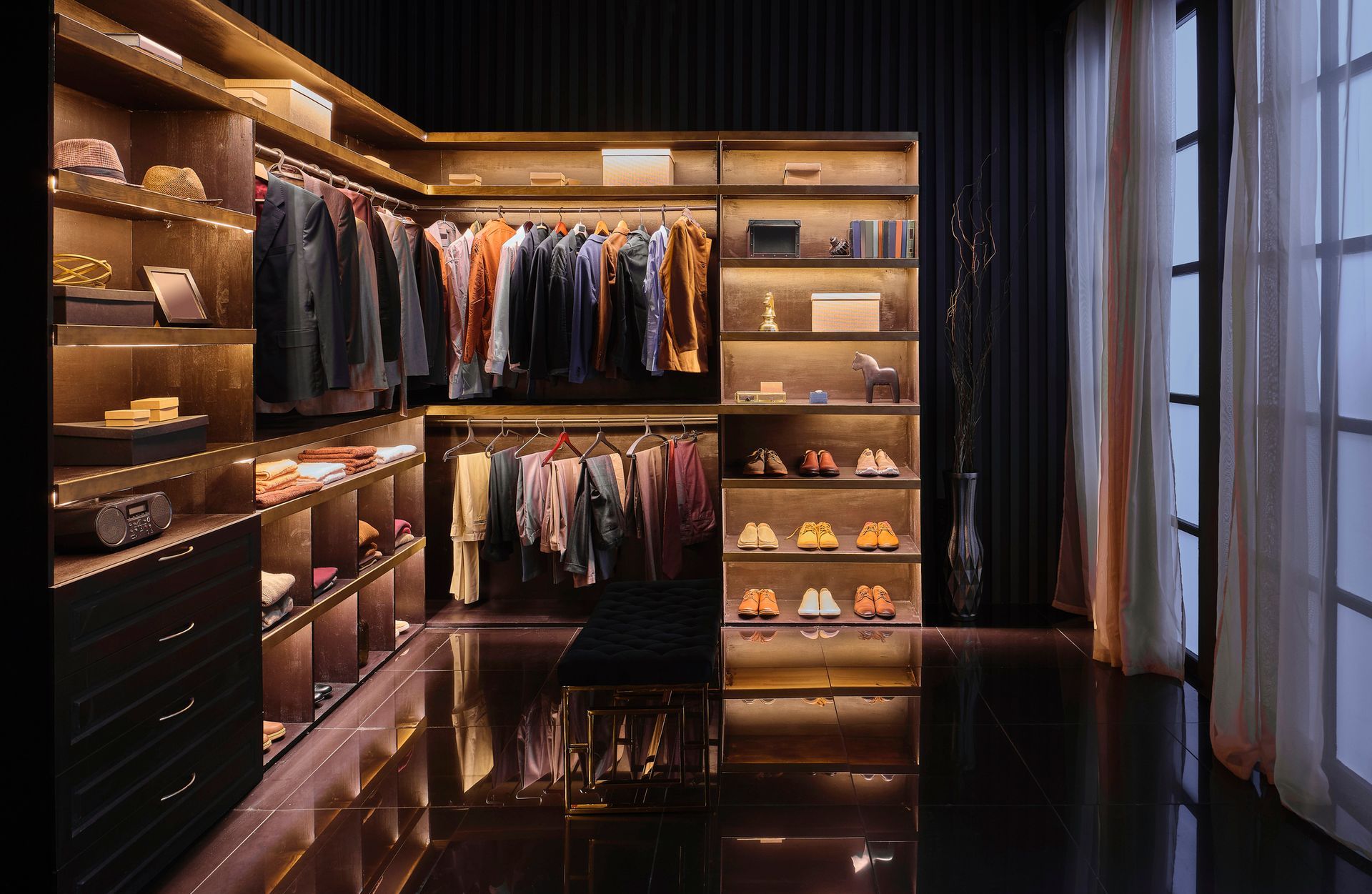 Luxurious walk-in closet with illuminated shelves and rows of clothing; black and brown tones, reflective floor.