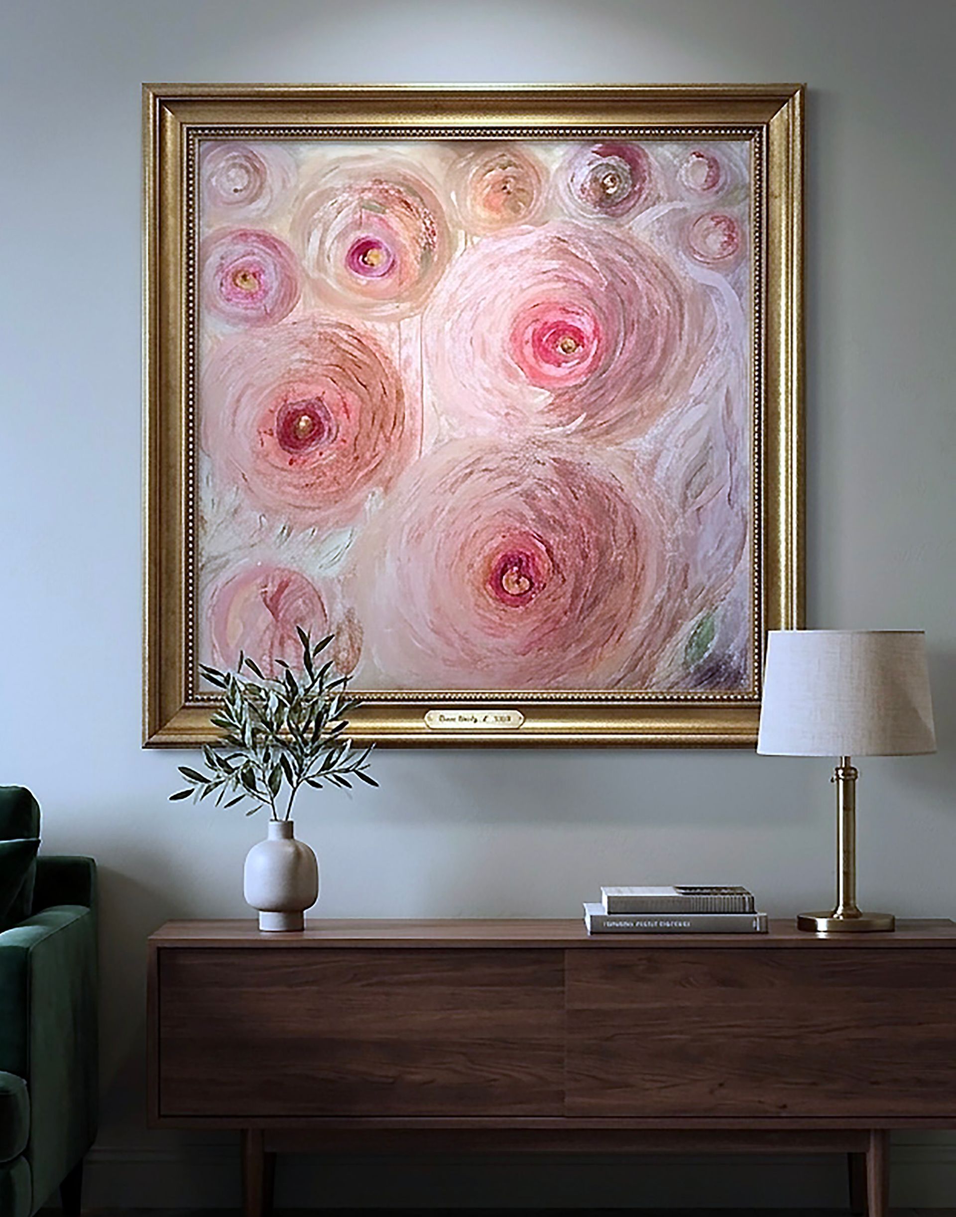 Ingelijst abstract roze bloemenschilderij boven een donkerhouten console met vaas, lamp en boeken.