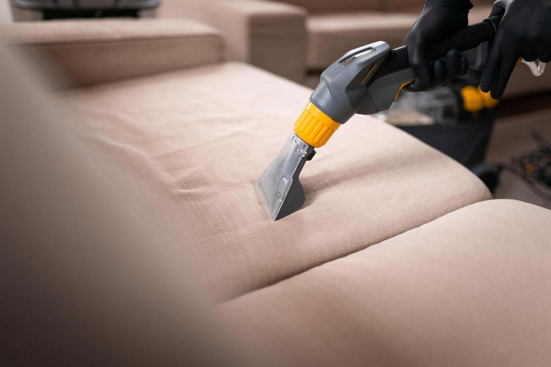 A person is cleaning a couch with a vacuum cleaner