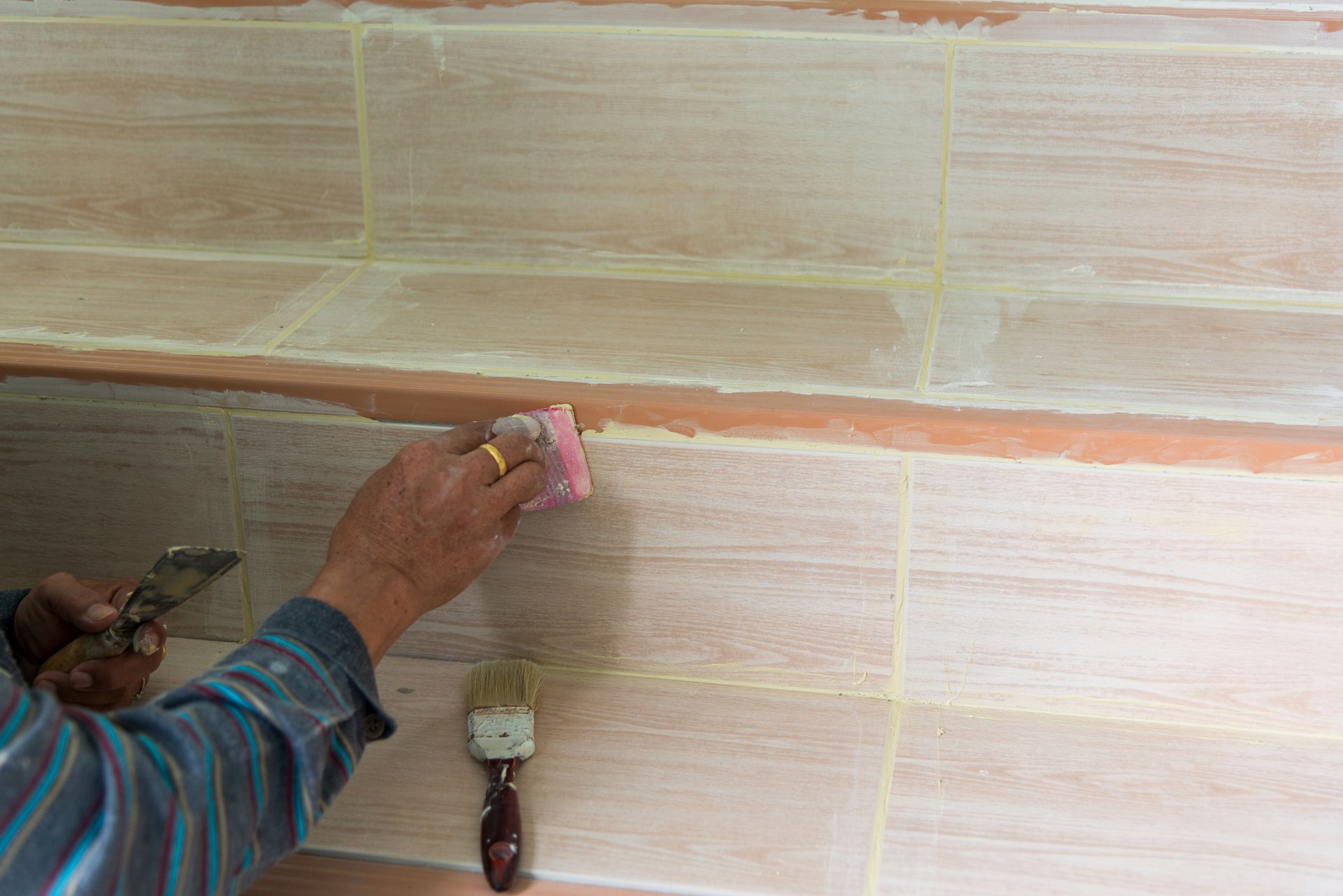 A man is painting a tile wall with a brush