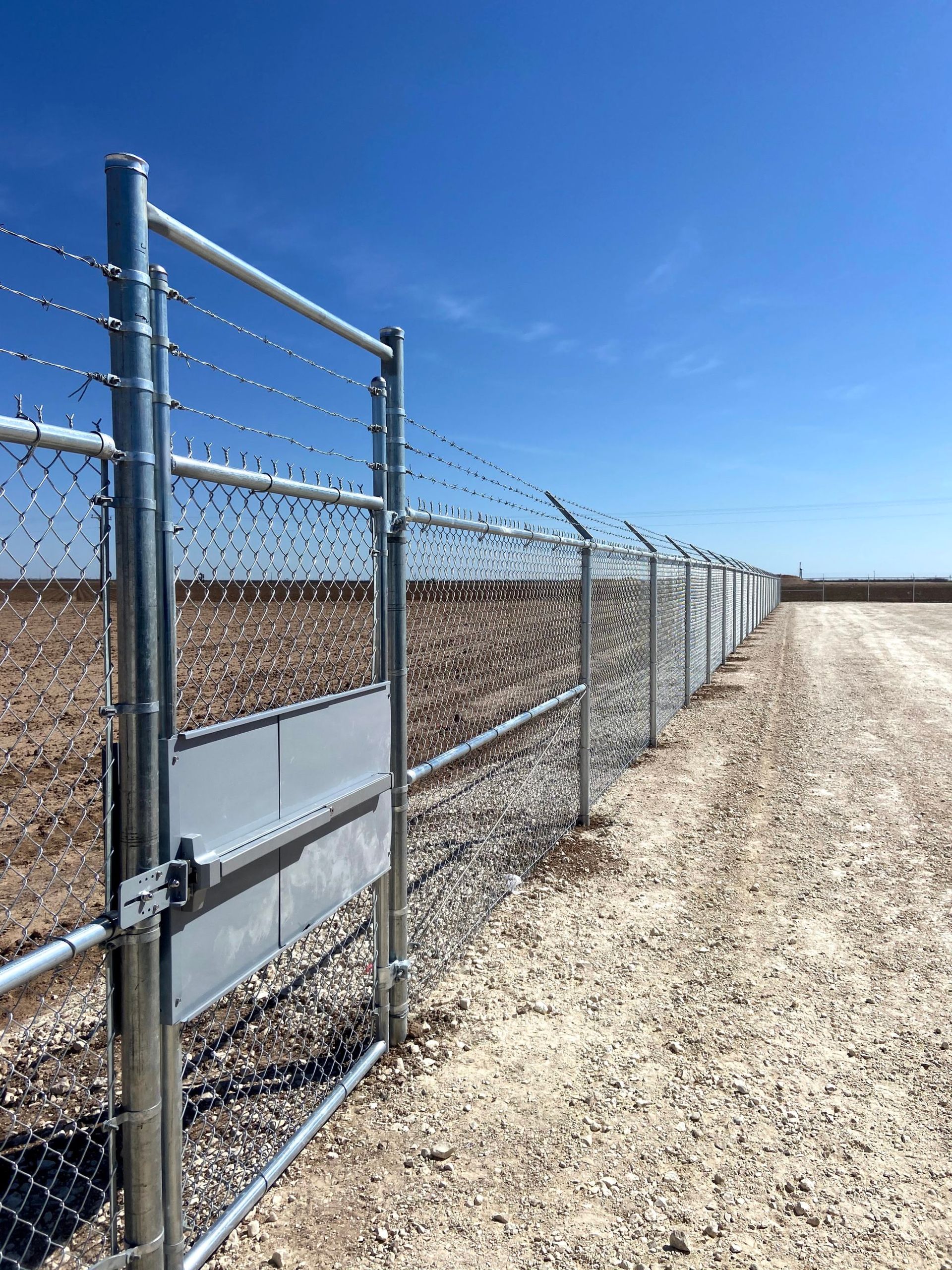 A barbed wire fence surrounds a dirt road in the desert.