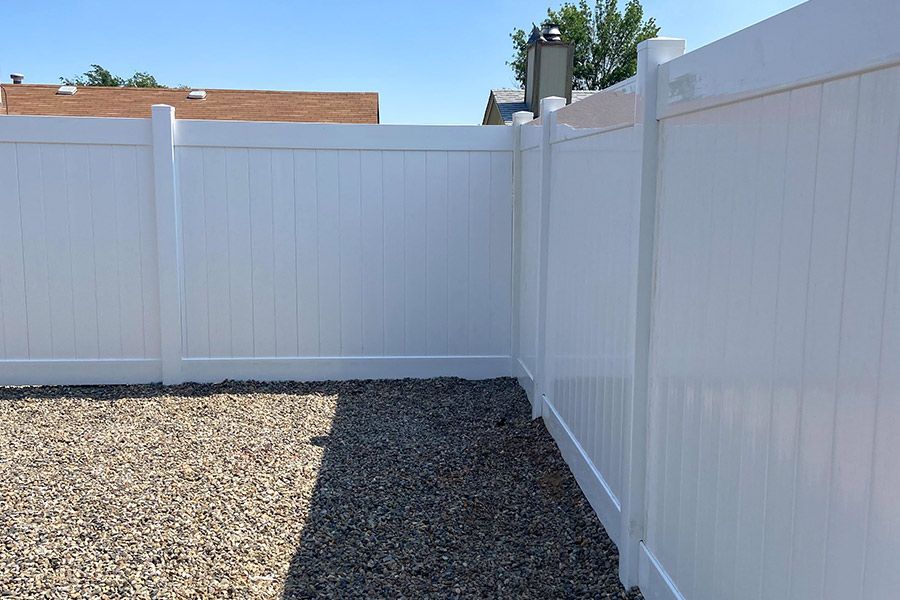 A white fence surrounds a gravel area in a backyard.