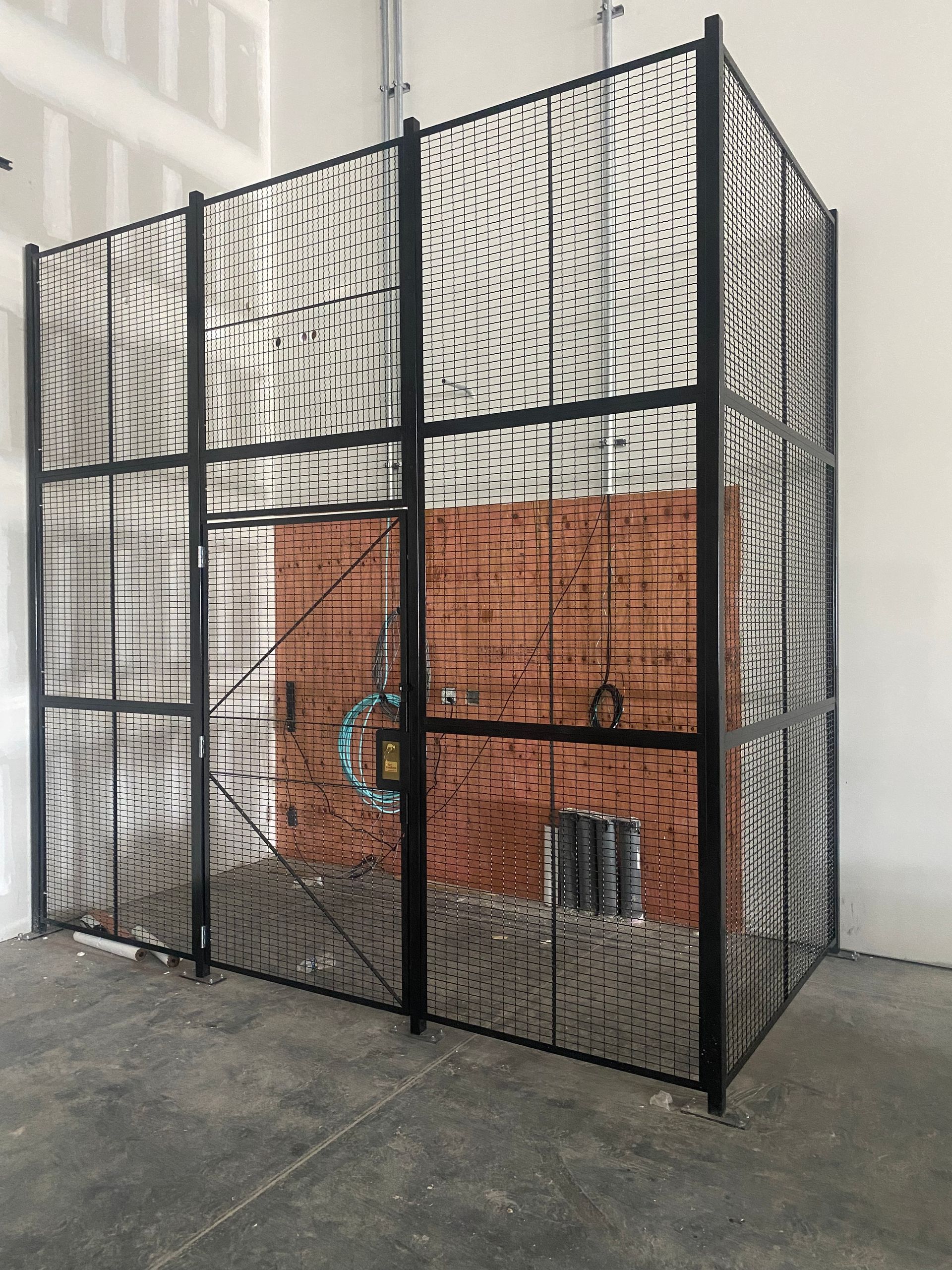 A black metal fence with barbed wire along the side of a dirt road.