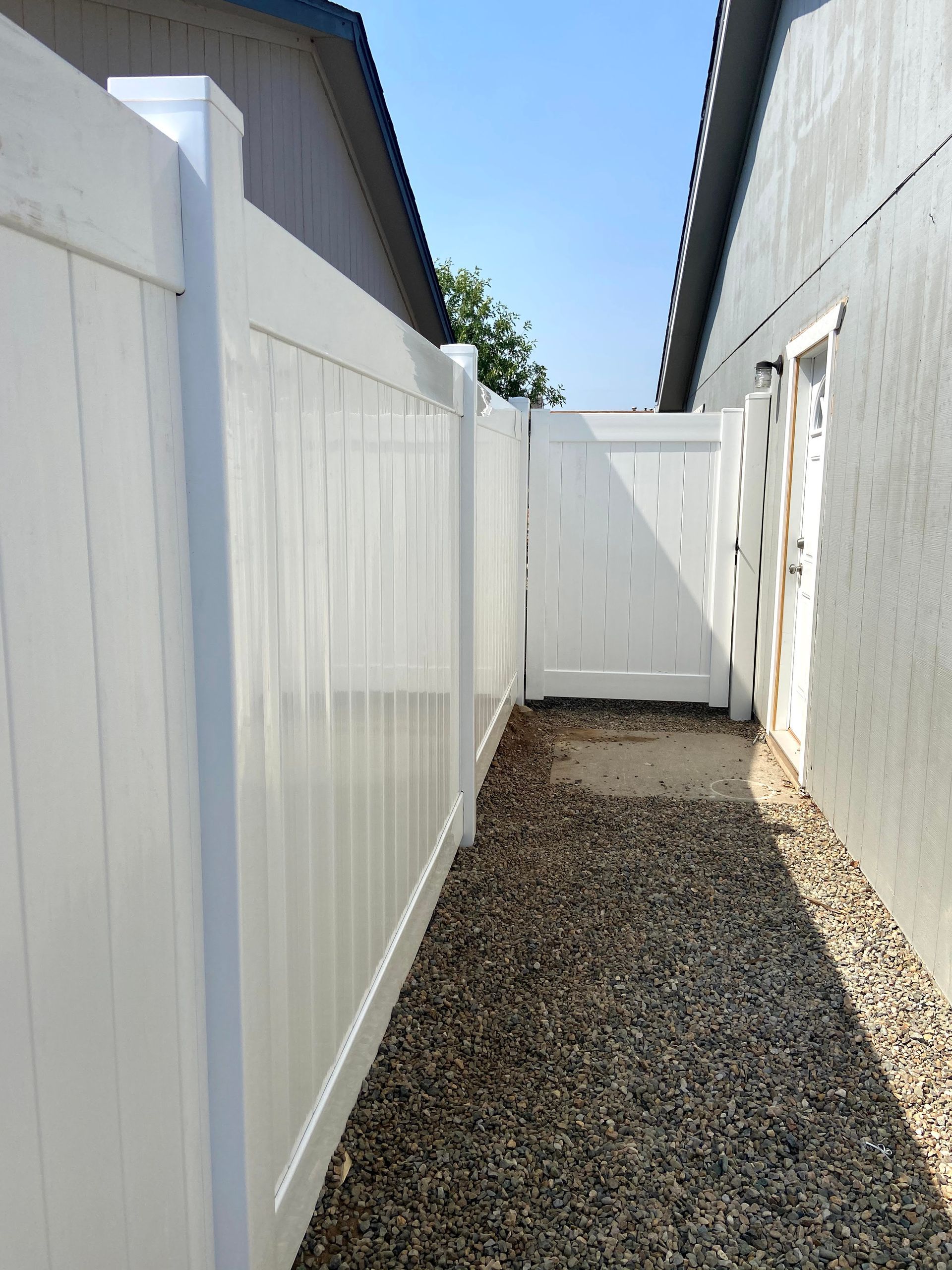 A white fence surrounds a gravel path between two houses.
