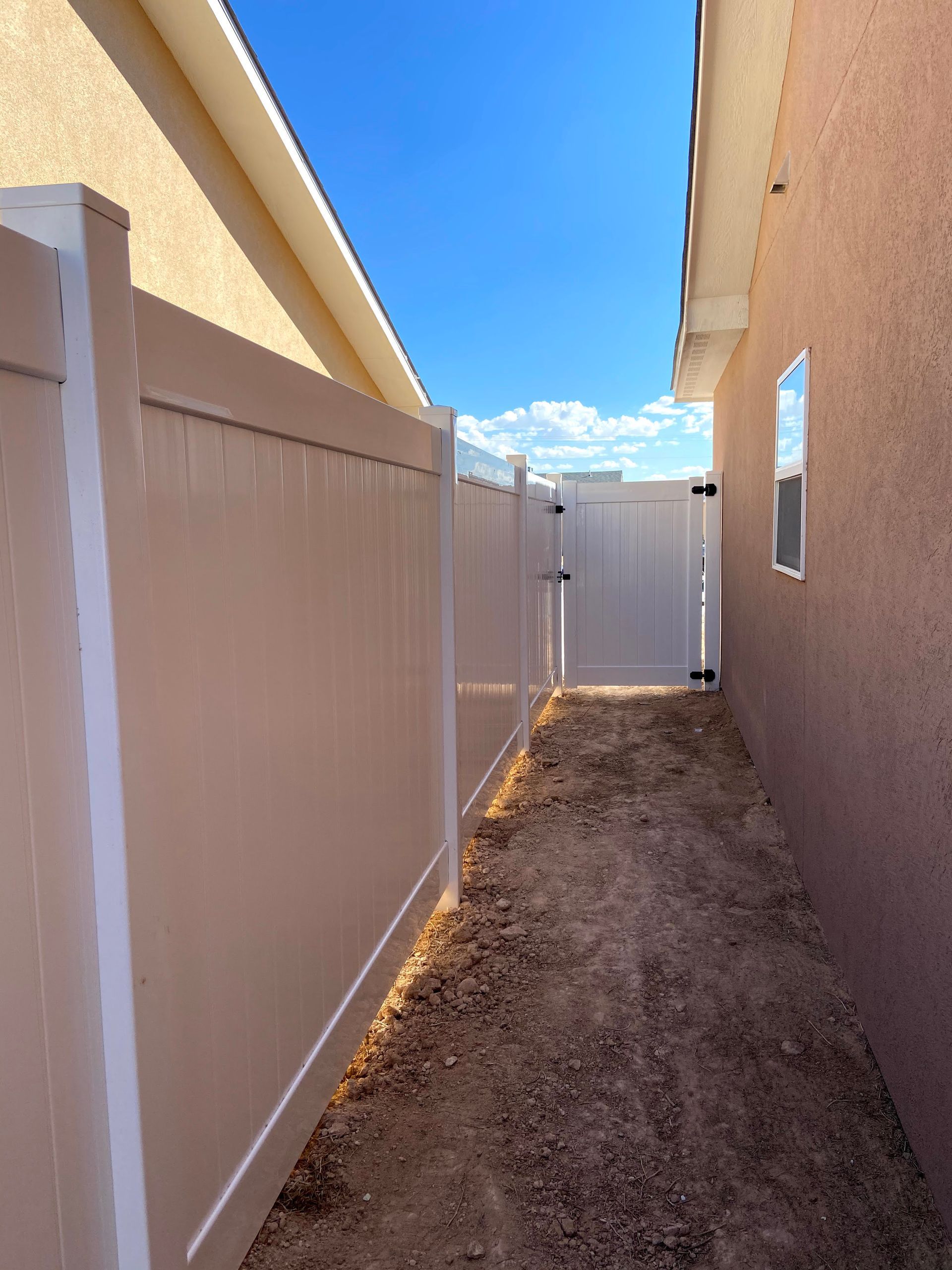 A white fence surrounds a dirt path leading to a house.