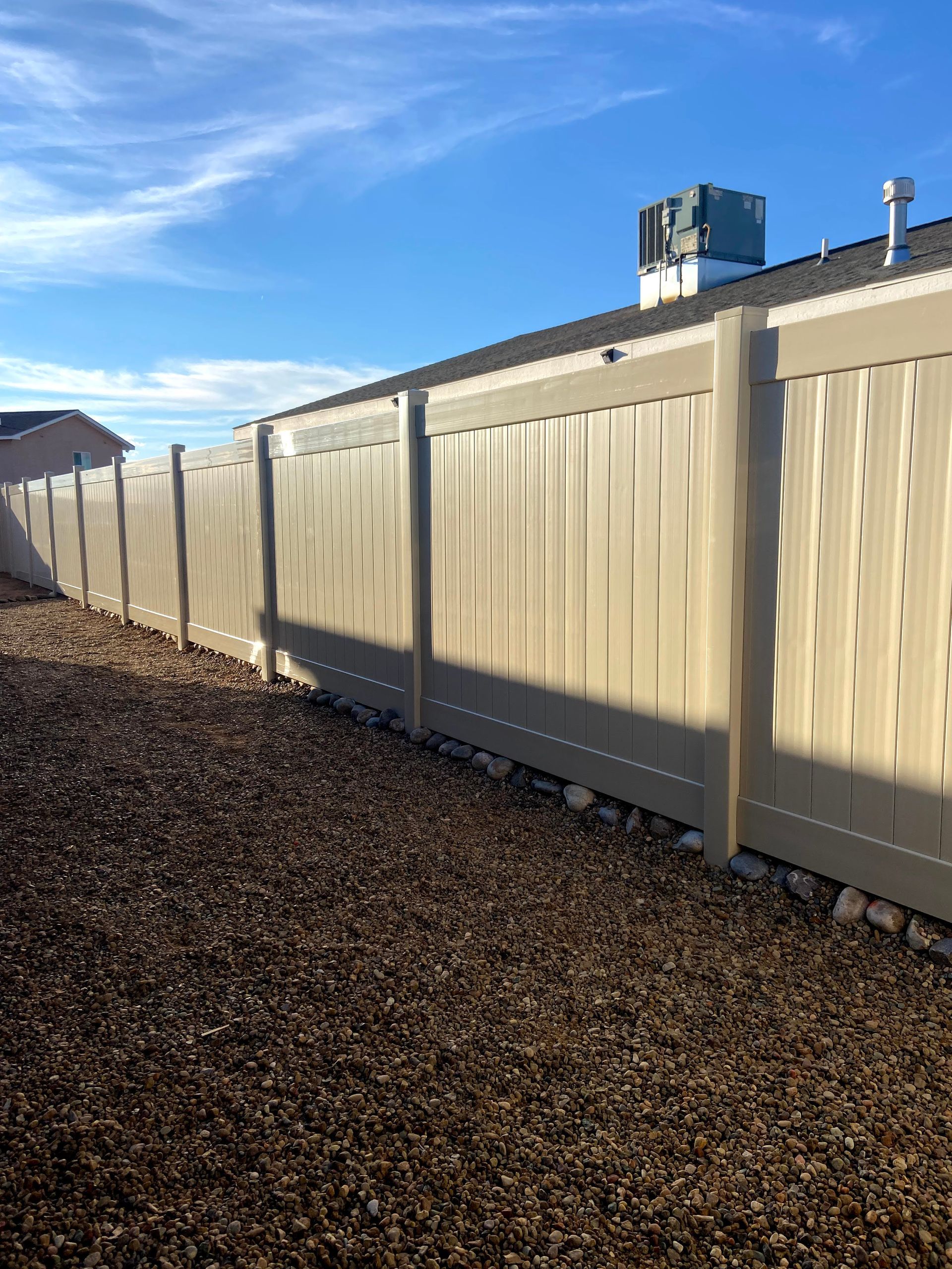 A white fence surrounds a gravel yard in front of a house.