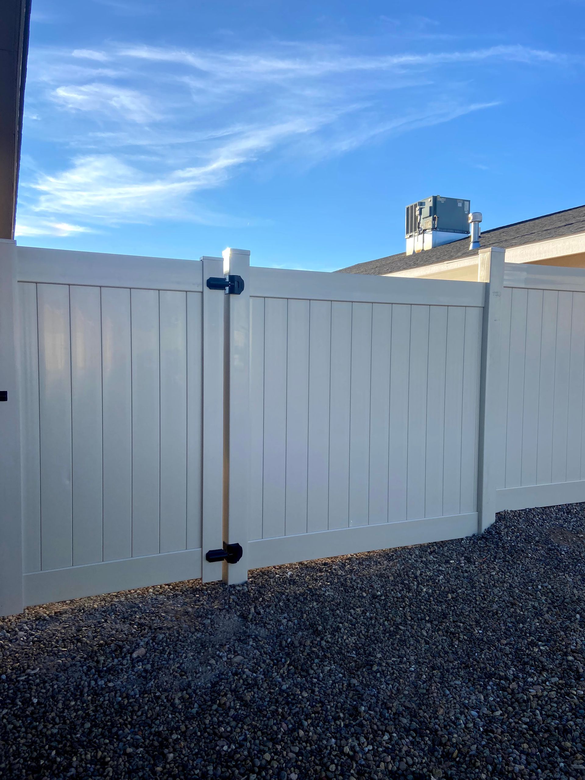 A white fence with a black gate and a blue sky in the background.