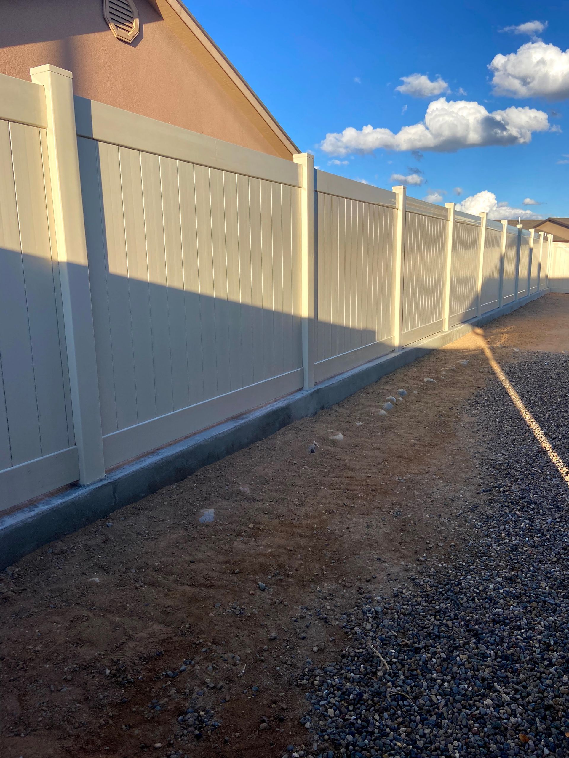 A white fence is sitting next to a gravel path in front of a house.