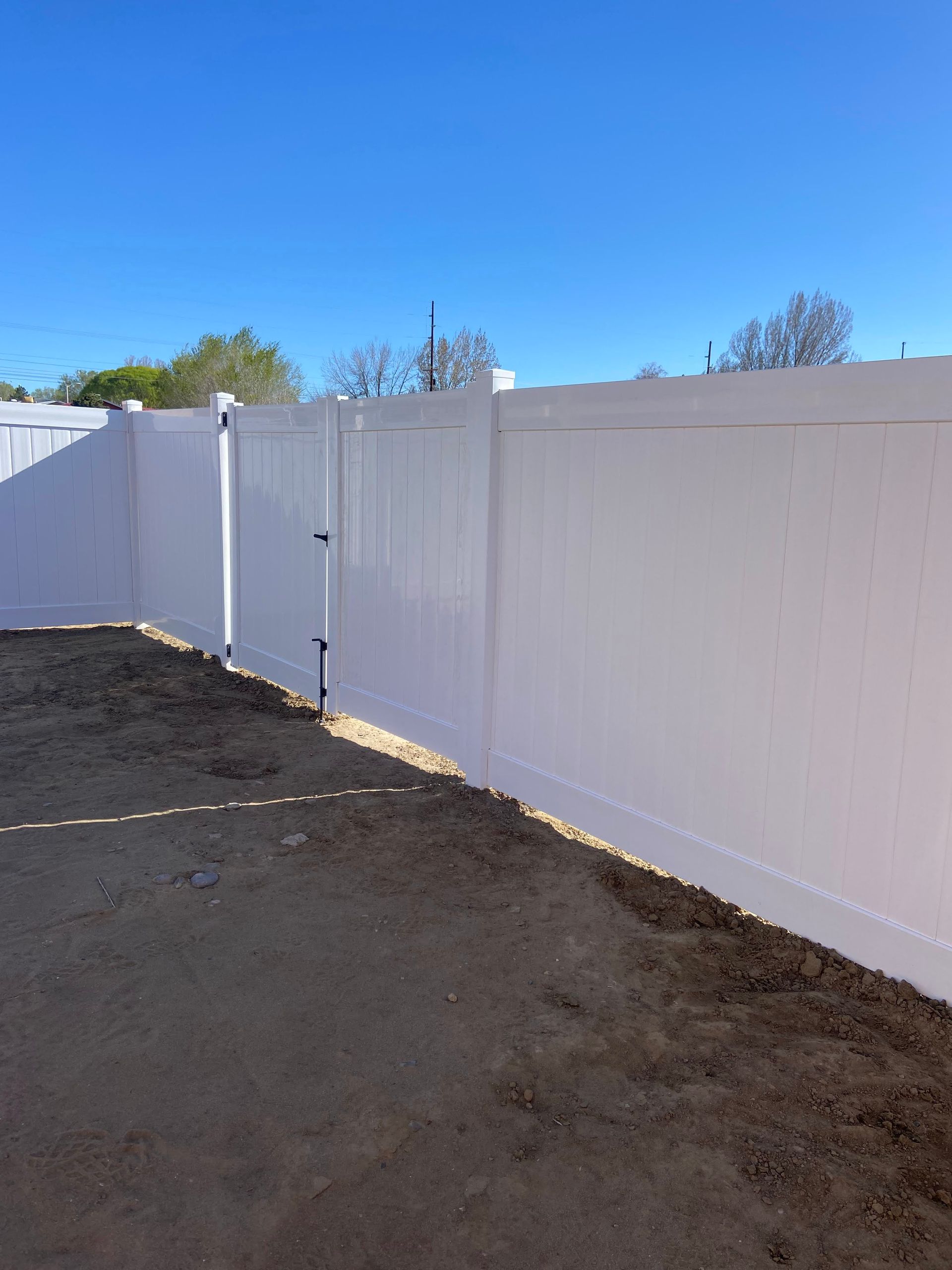A white fence surrounds a dirt area with a blue sky in the background