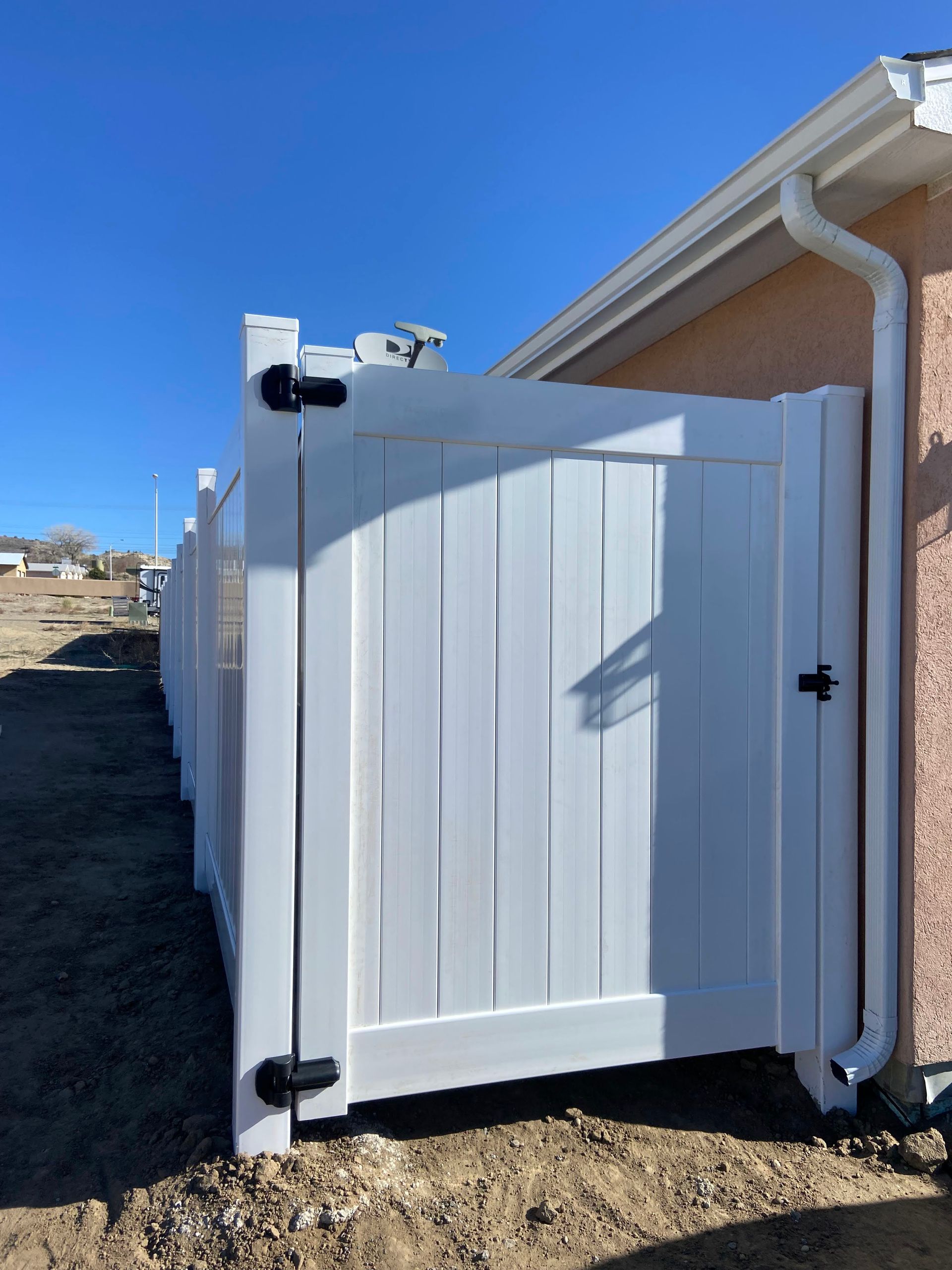 A white fence with a black gate is next to a house.
