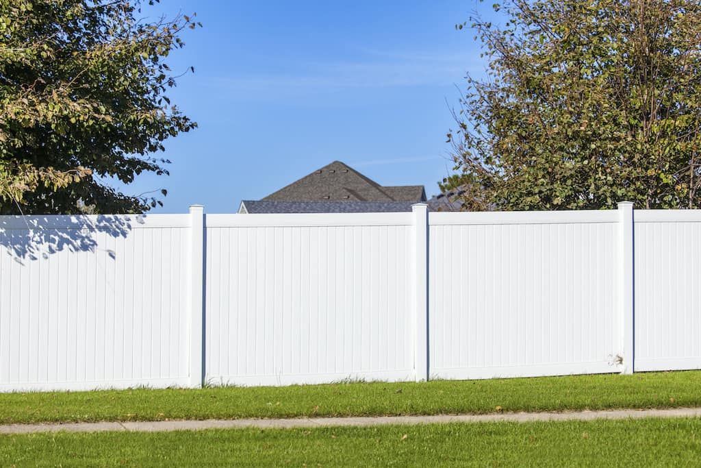 A white fence surrounds a lush green yard with a house in the background.