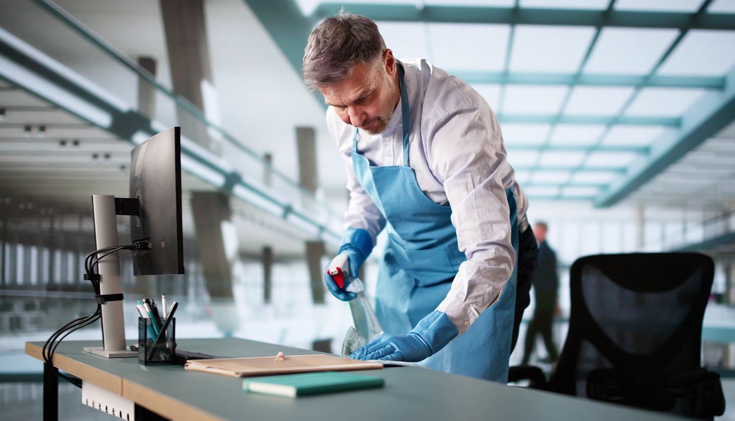 Person in blue apron cleaning a desk in an office.