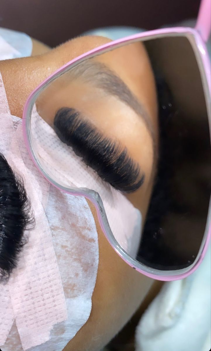 Close-up of an eye with long false eyelashes reflected in a pink-framed heart-shaped mirror