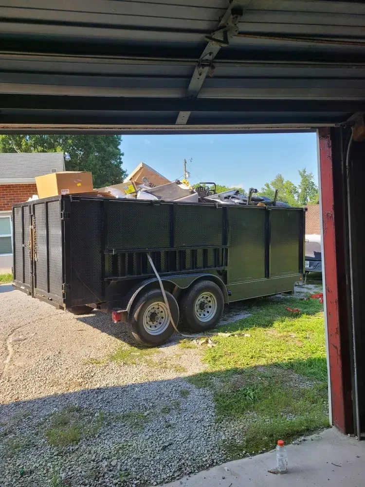A dumpster trailer is parked in front of a garage door.