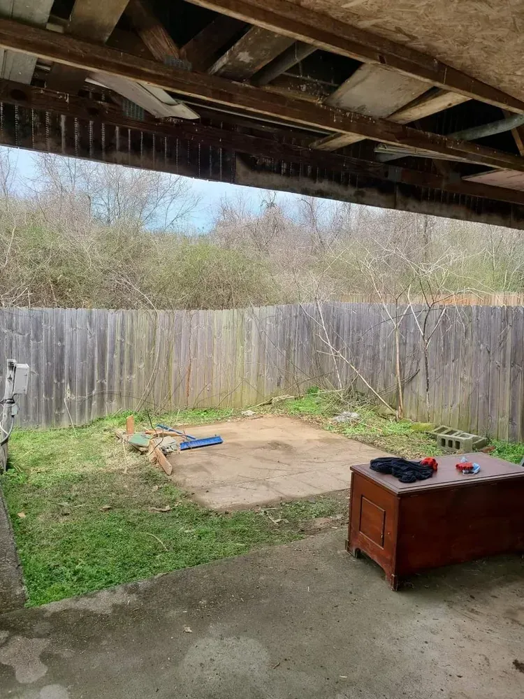 A backyard with a wooden fence and a table under a covered patio.
