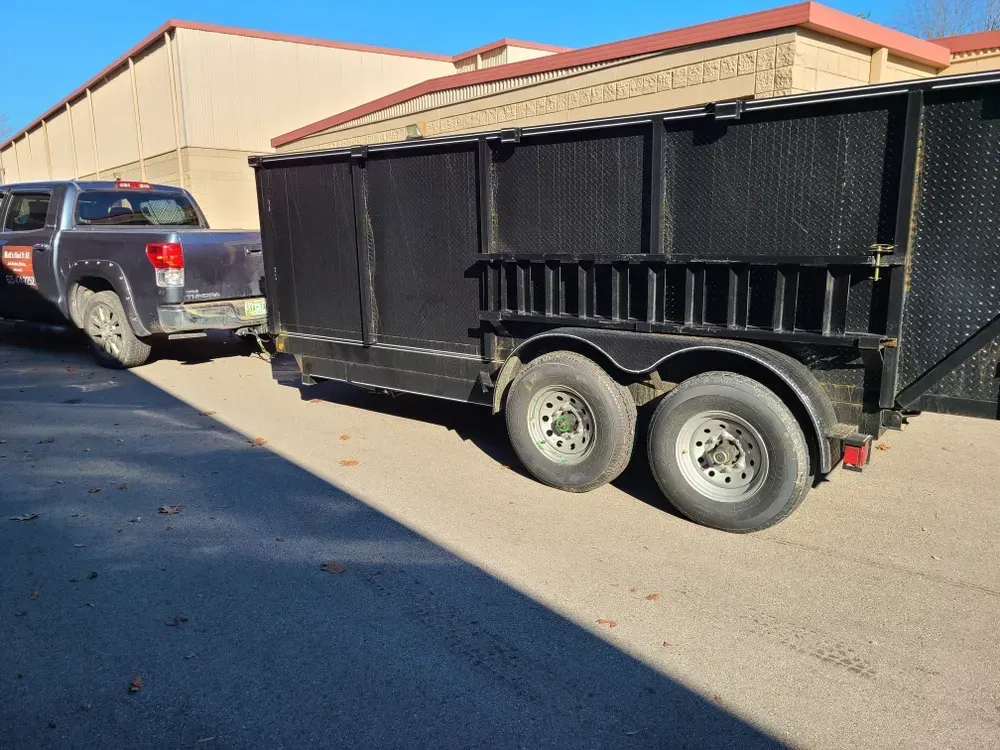 A truck is towing a black trailer with a ladder attached to it.