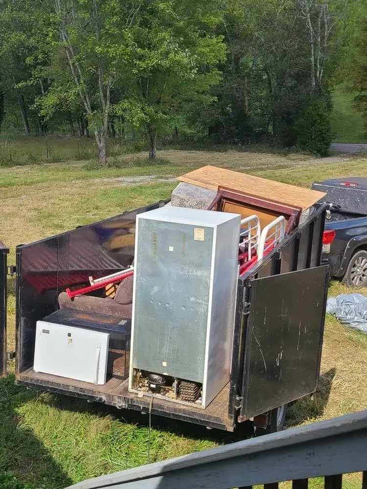 A dumpster filled with junk is parked in a grassy field.
