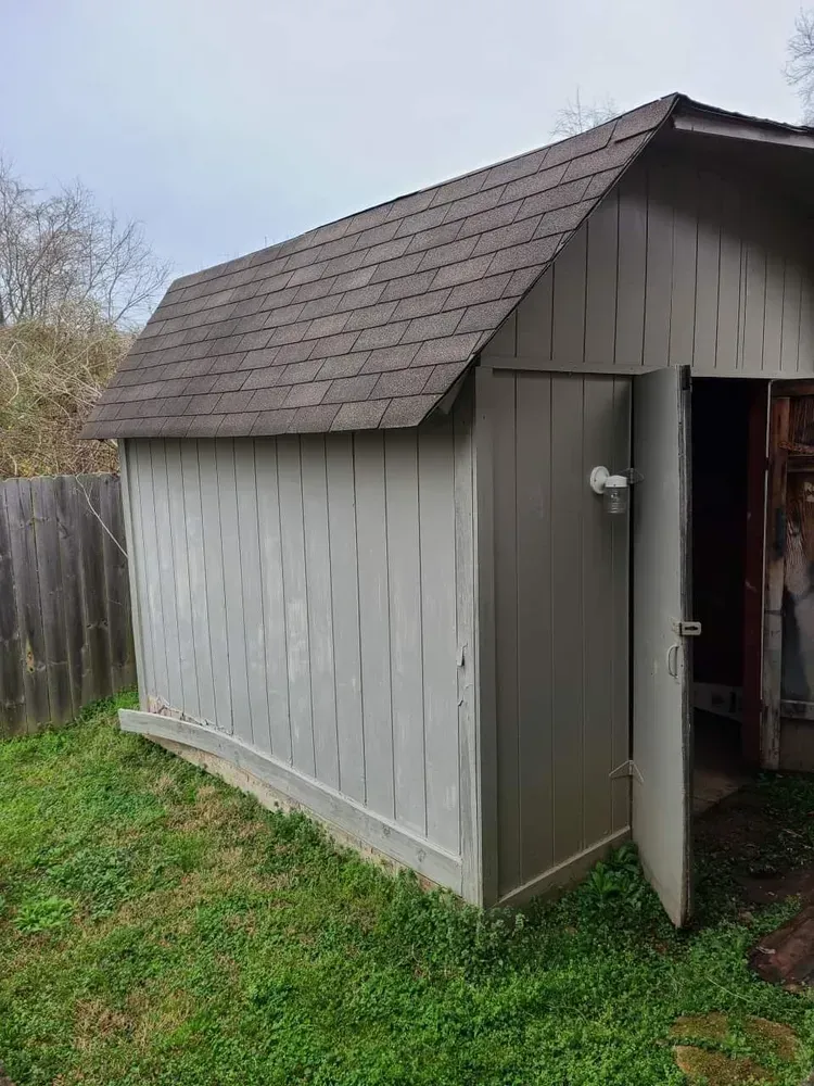A gray shed with a brown roof is sitting in the grass in a backyard.