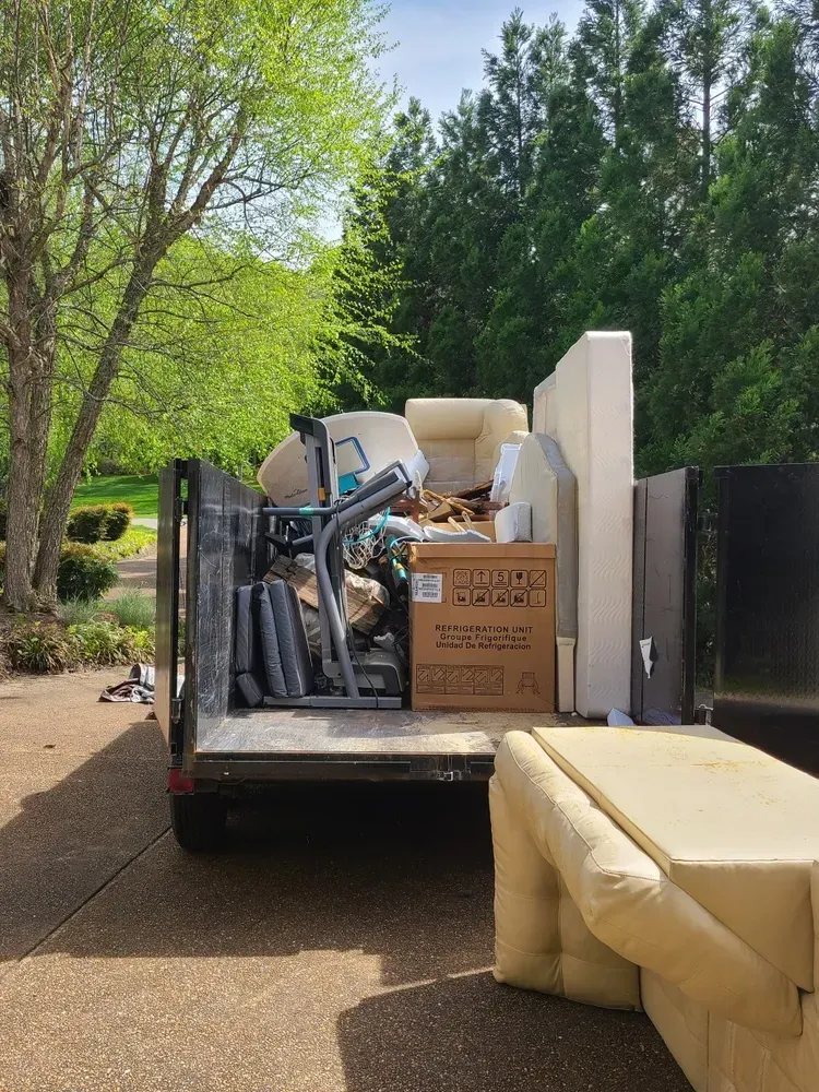 A dumpster filled with furniture and boxes is parked in a driveway.
