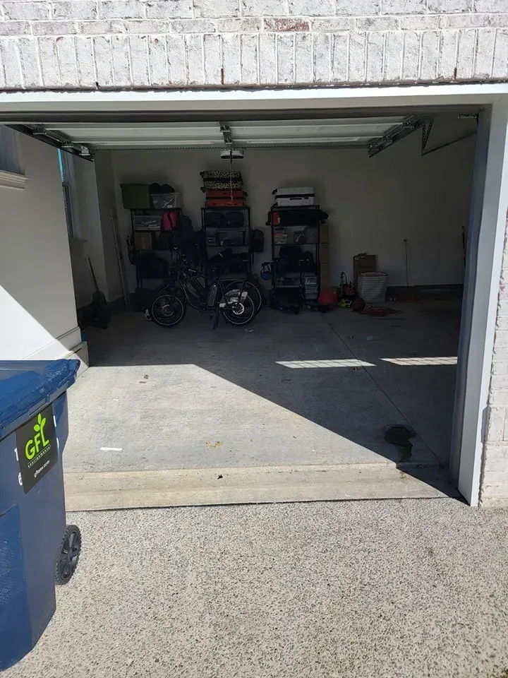 A garage with a blue trash can in front of it.