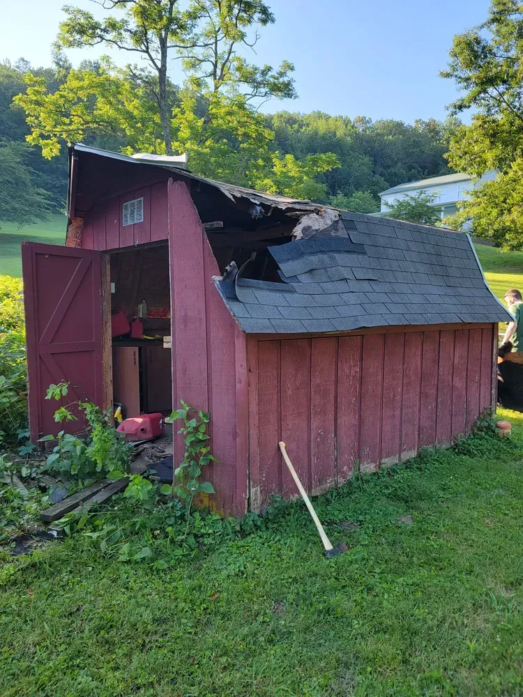 A red shed with a roof that has been damaged by a fire.