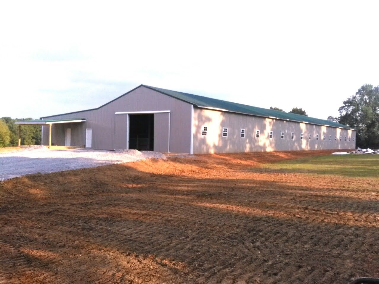 A large building with a green roof is sitting in the middle of a dirt field.