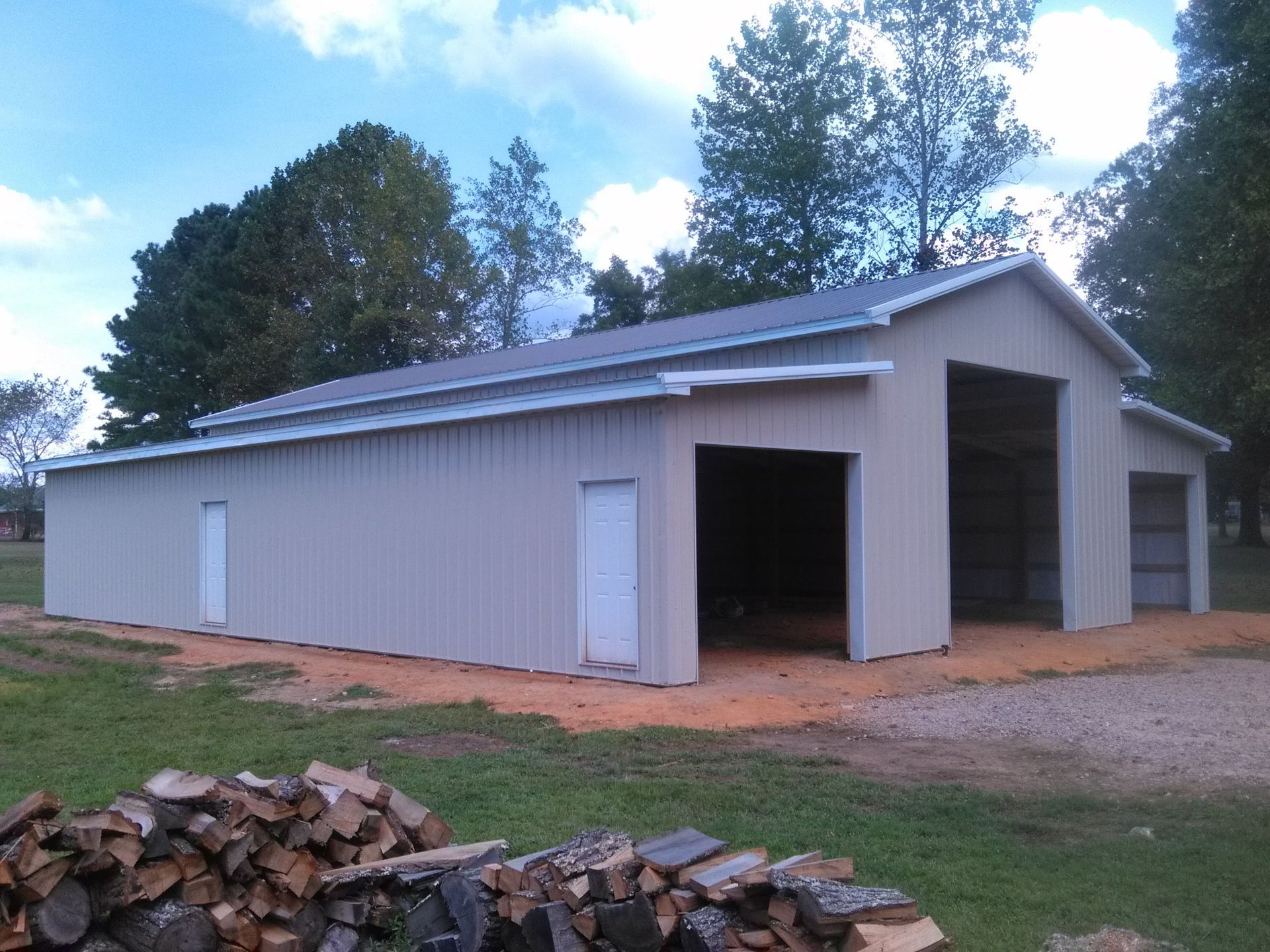 A large barn with a lot of doors and a pile of logs in front of it