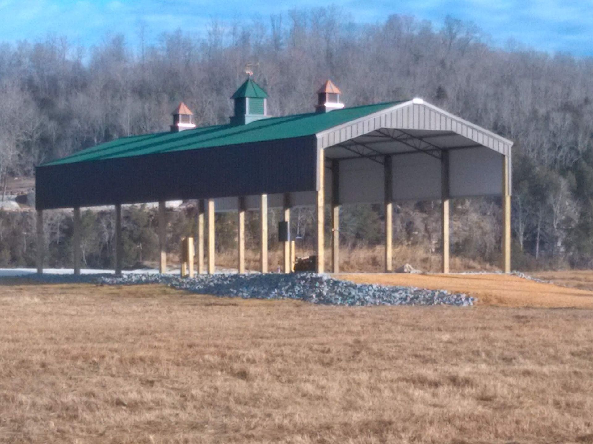 A large metal building with a green roof is sitting in the middle of a field.