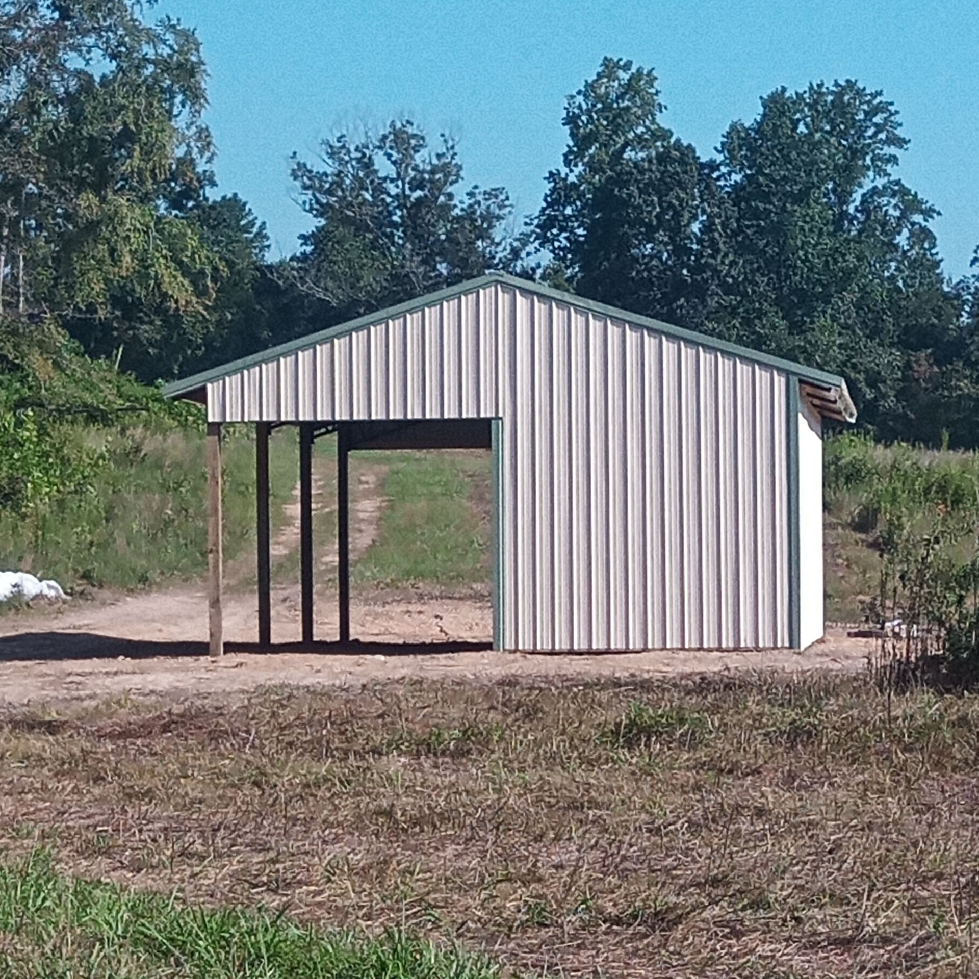 A white building with a green roof is in the middle of a field