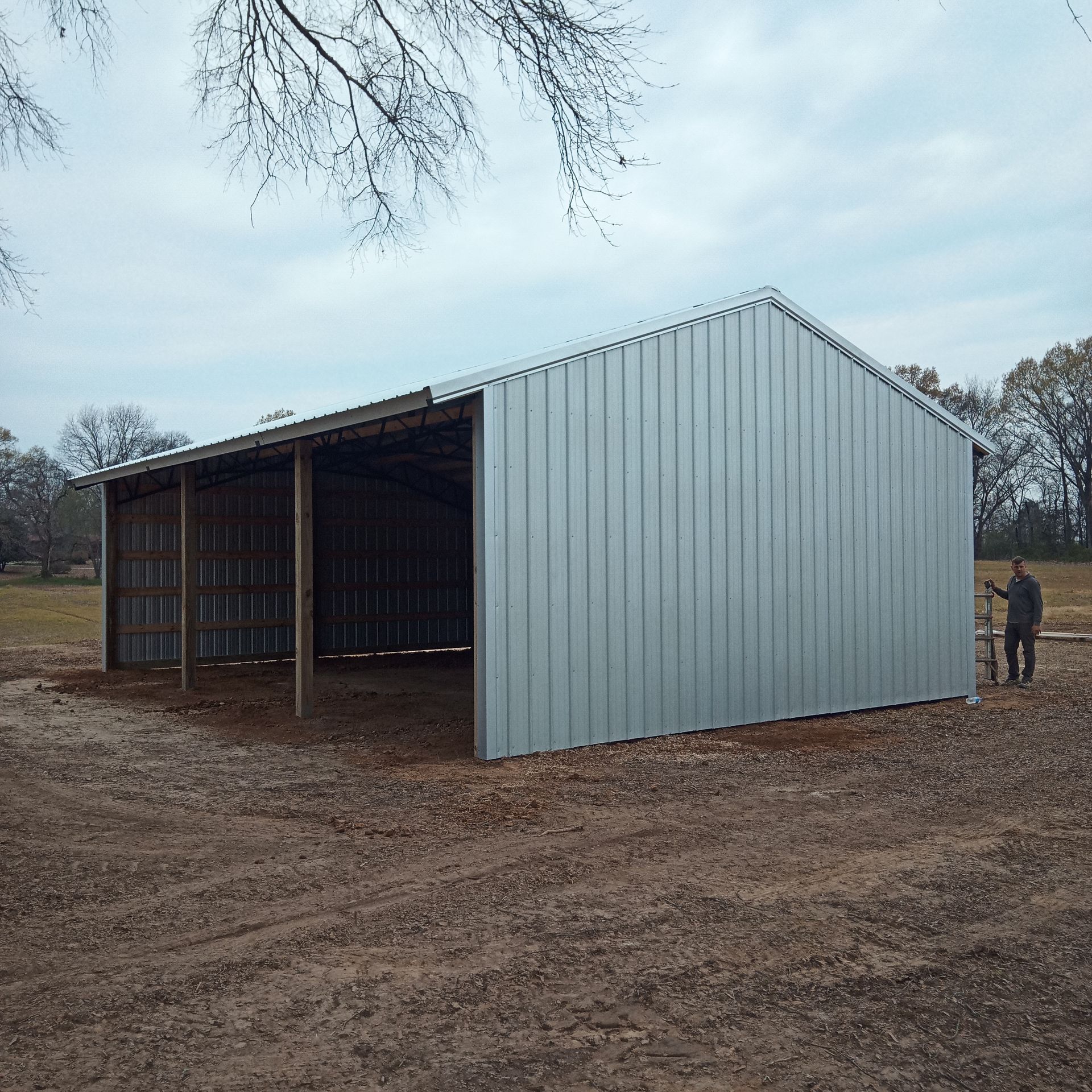 A man stands in front of a large metal building