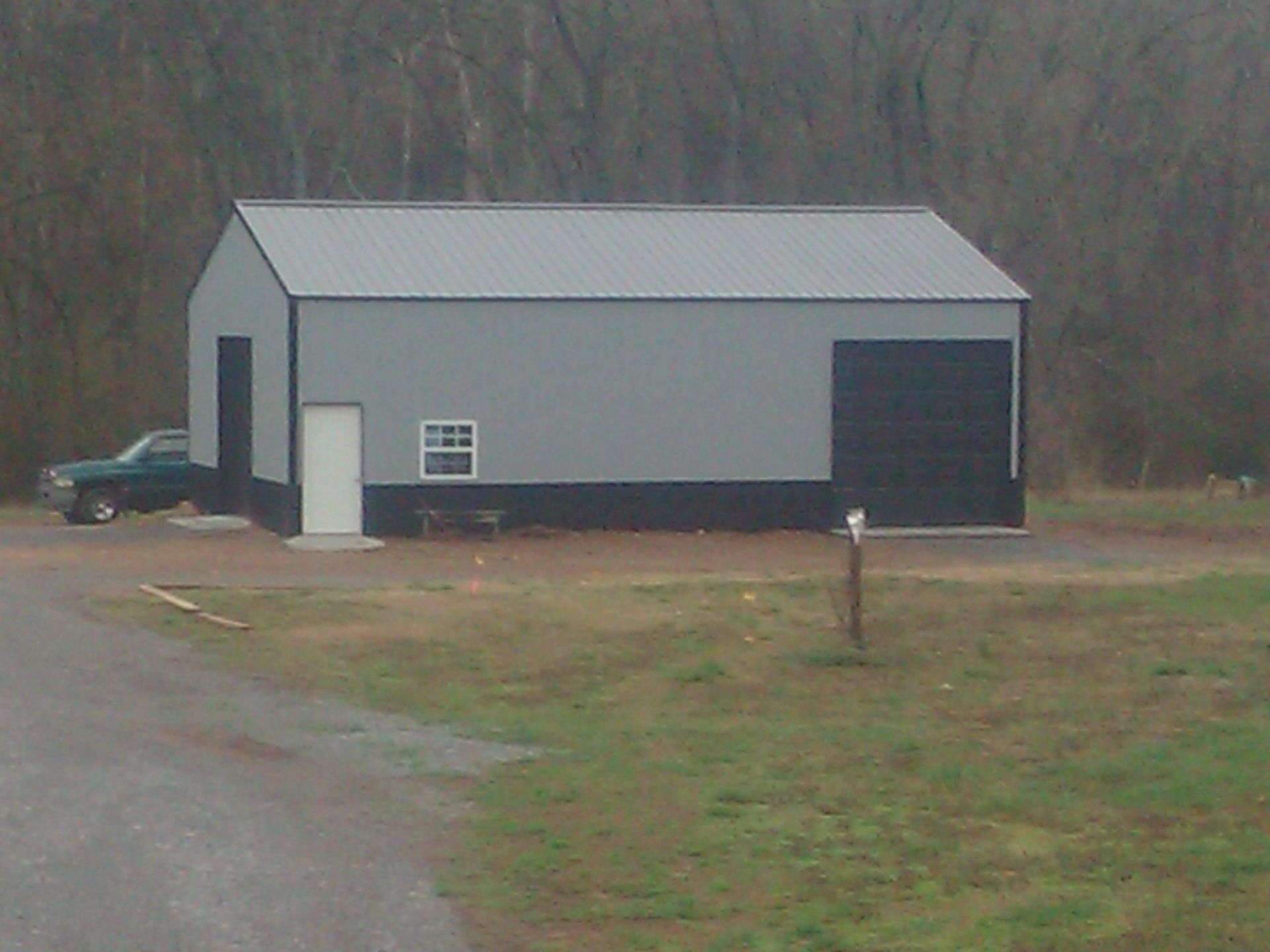A gray and black garage with a green truck parked in front of it.